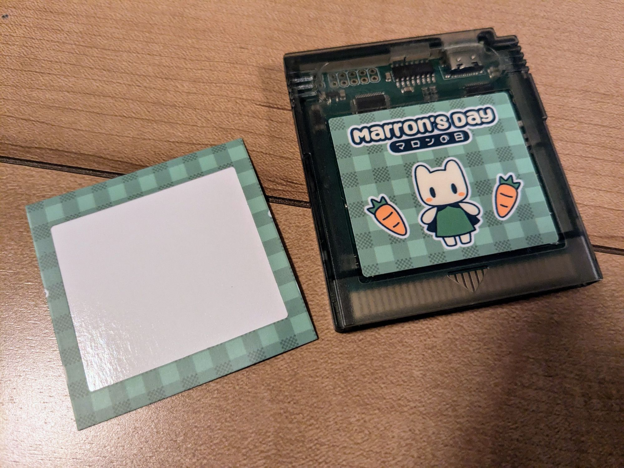 empty sticker sheet next to translucent black gameboy cartridge with the sticker for marron's day on it!