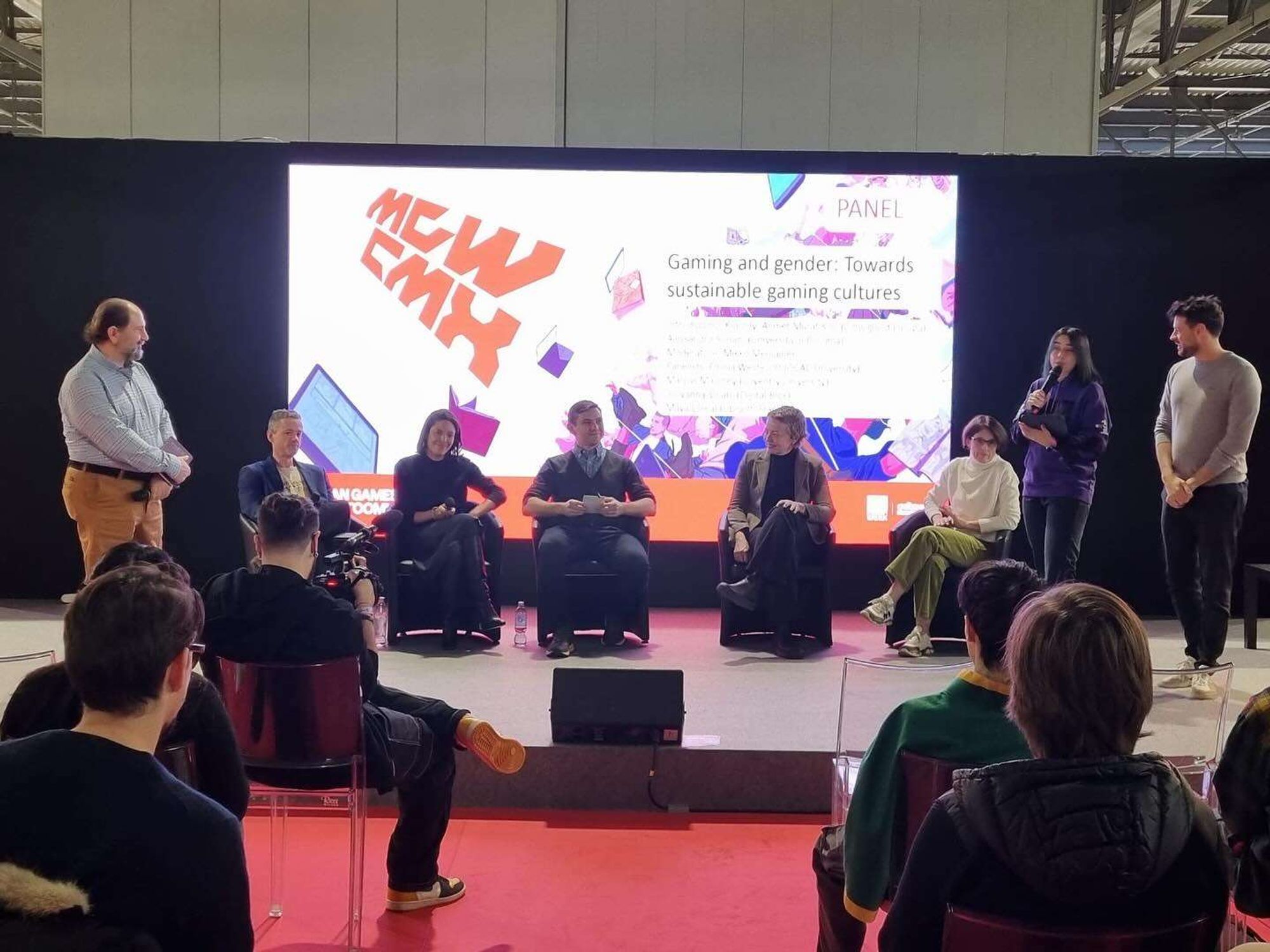 Photo of people on stage in a discussion panel. Behind them is a screen that reads "Gaming and gender: Towards sustainable gaming cultures".