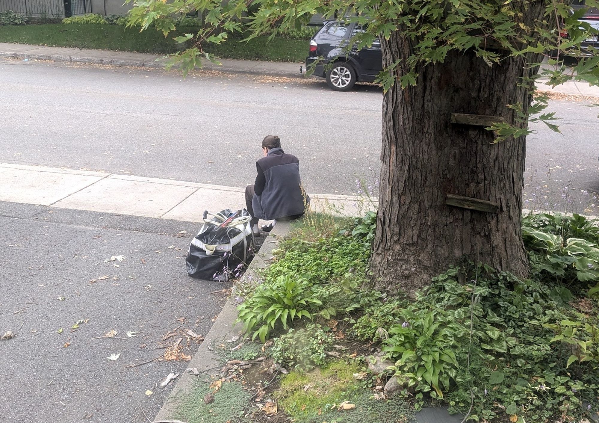 A teenager with hockey gear, waiting by the side of the road for the lift to the game.