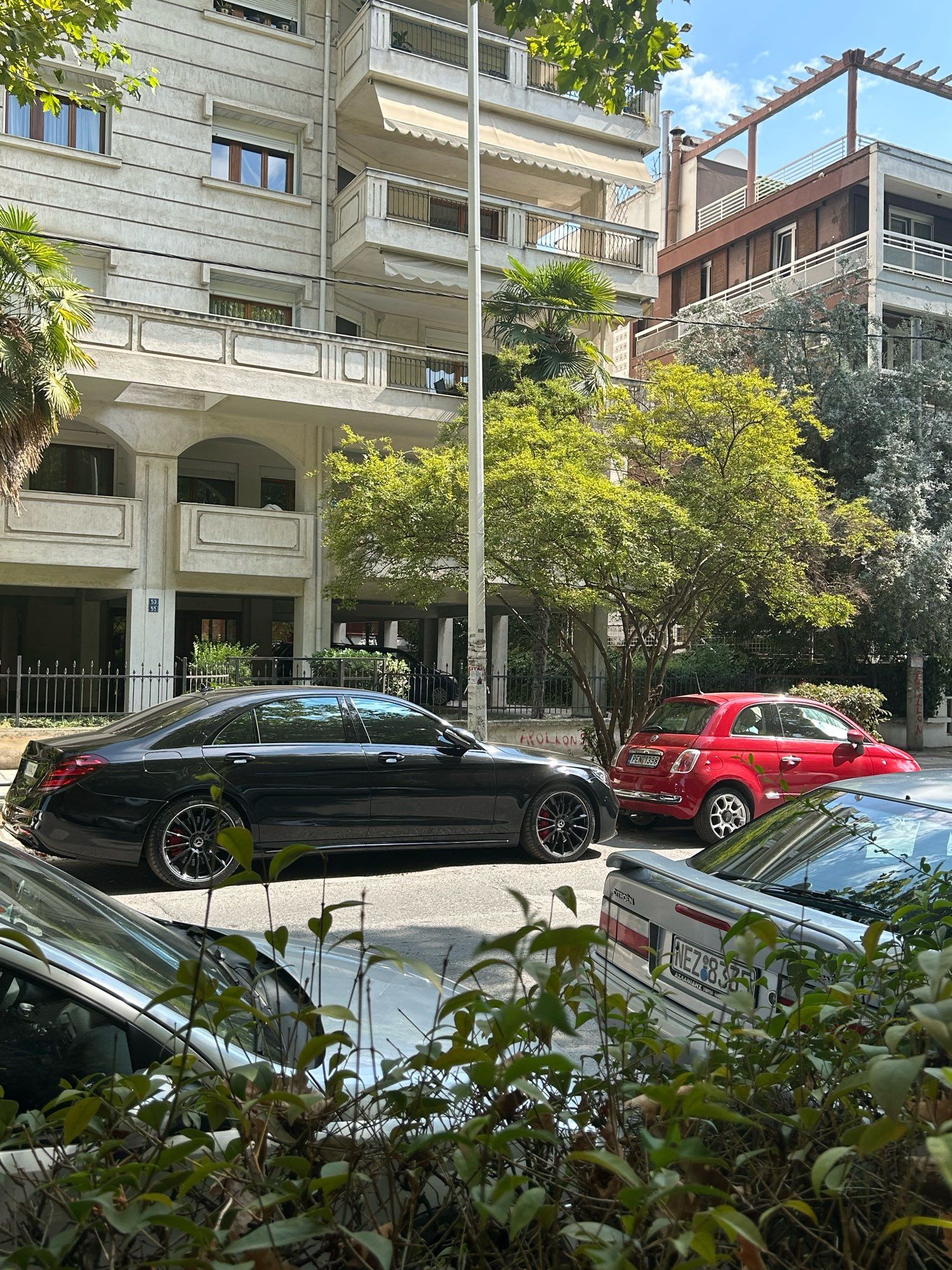 A black Mercedes parked behind a red Fiat 500, across the street from a Citroen Xantia