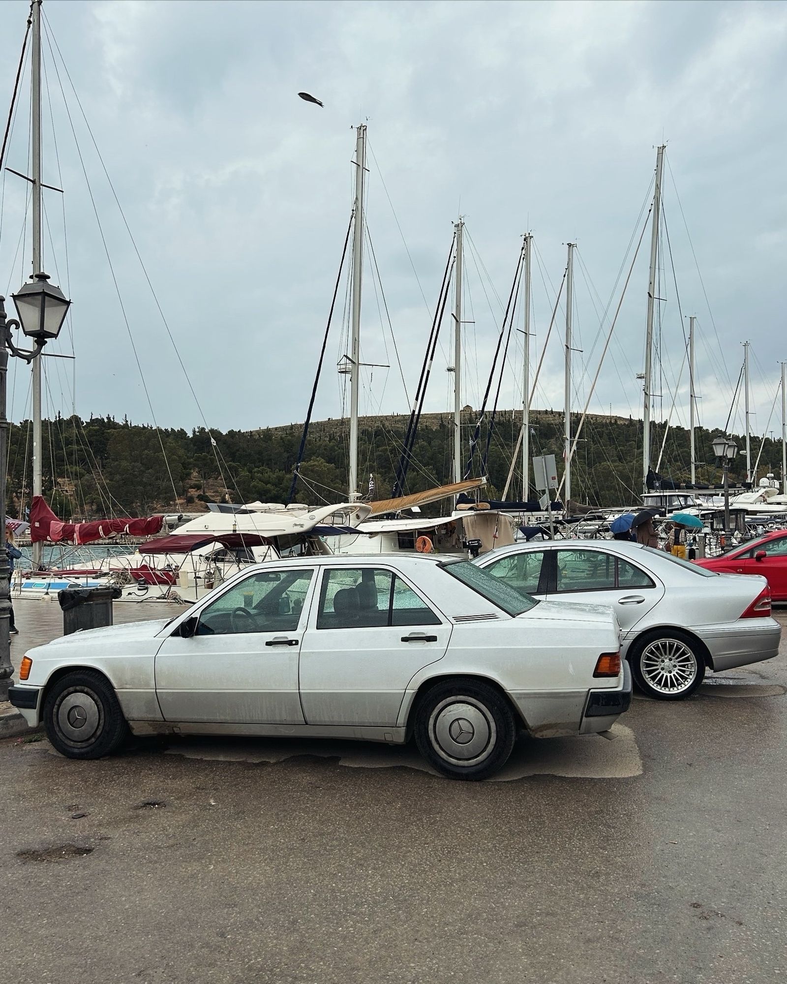 A white W201 190E parked next to a silver W203 at a Marina parking spot at Galaxidi