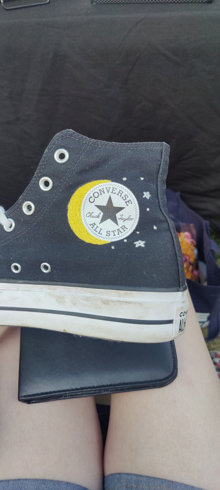 Otherside of a converse shoe with a moon around the left side of the logo with stars and white dots on the left