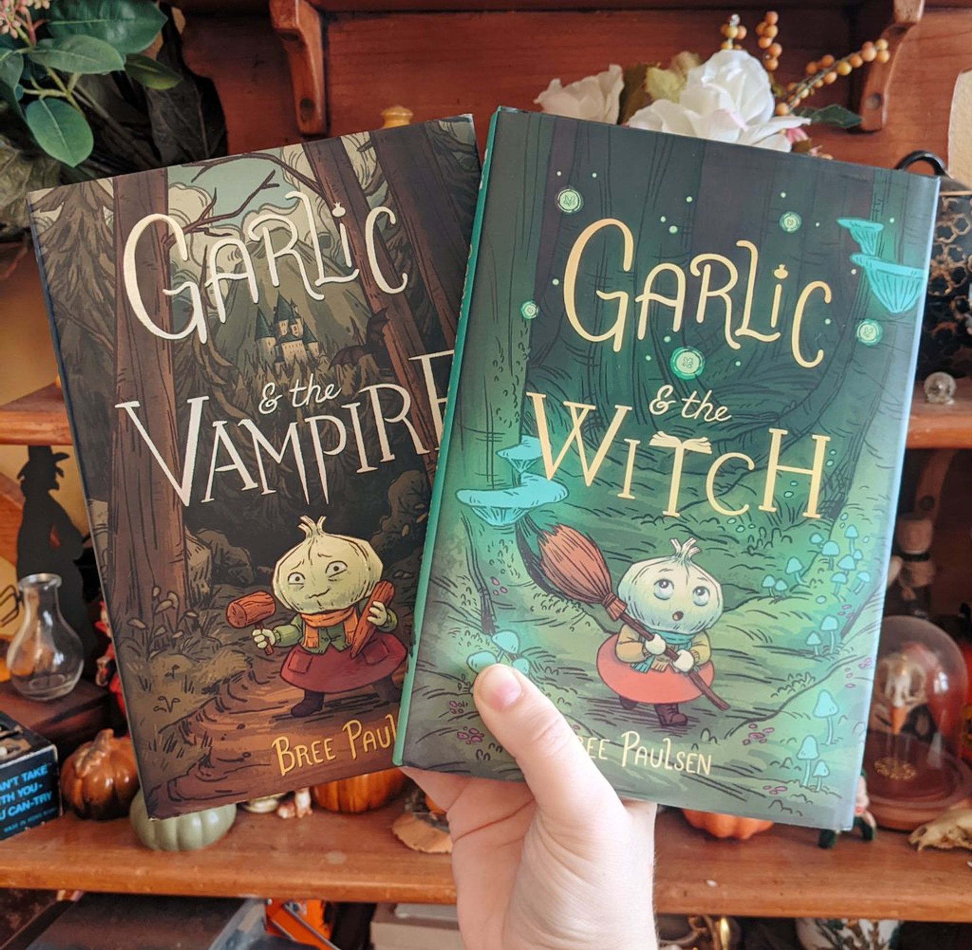 hand holds up two graphic novels: Garlic & the Vampire, Garlic & the Witch