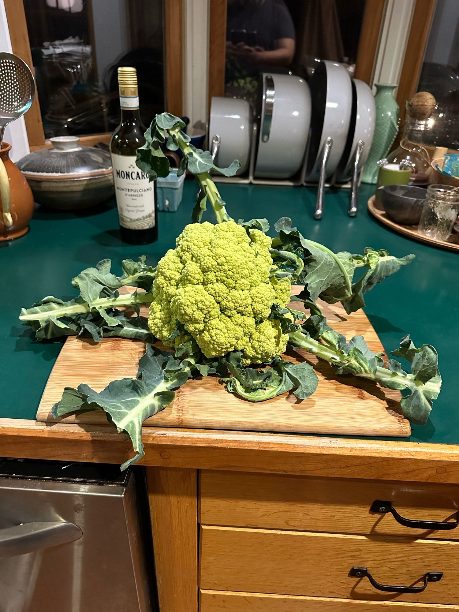 A cauliflower broccoli hybrid that looks like a pale green cauliflower but not the classic one with spirals, seated on a wooden cutting board.