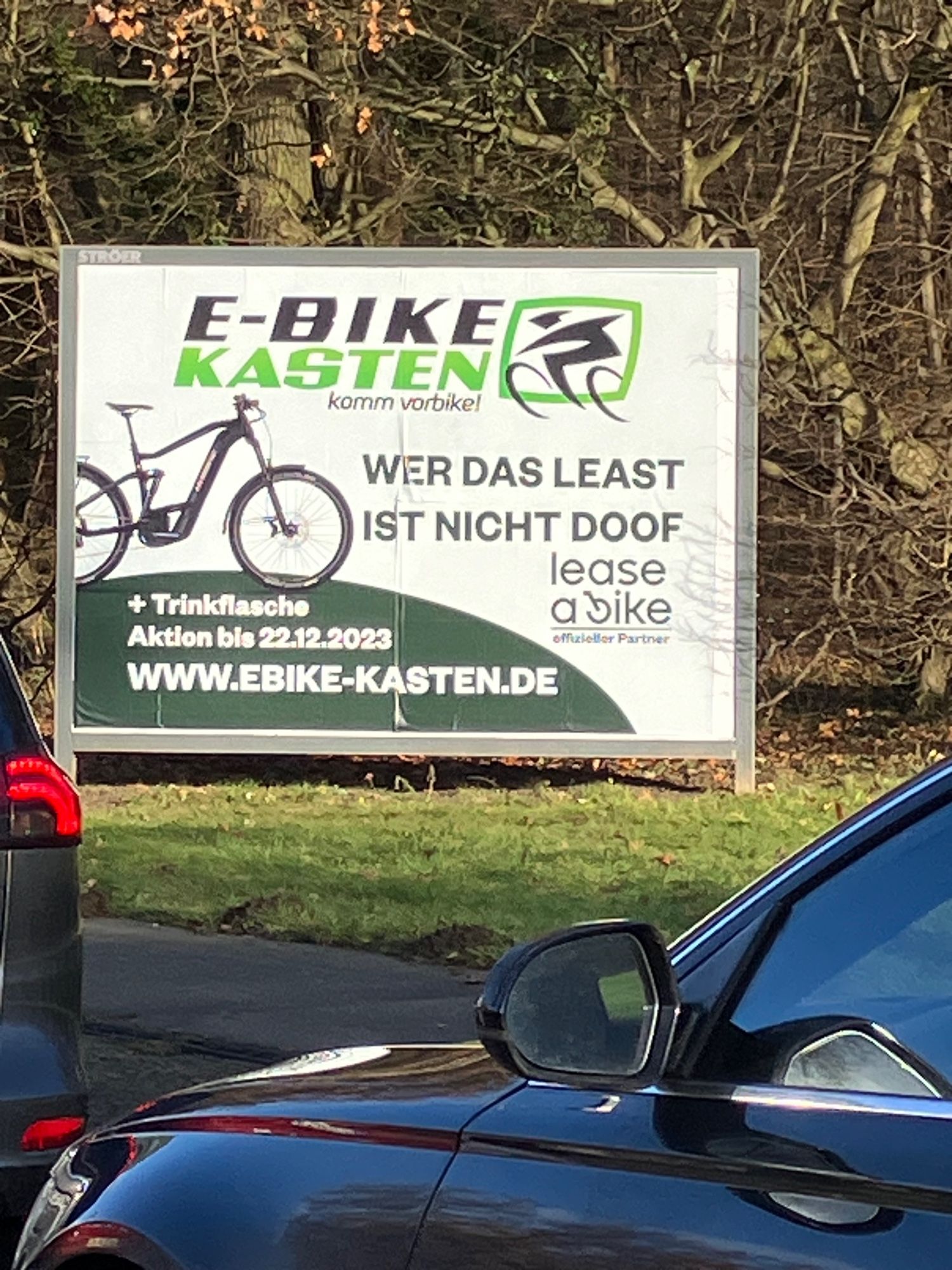 Werbeplakat für einen E-Bike-Händler mit einem E-Bike und dem Spruch „Wer das least (englisch geschrieben) ist nicht doof.“  Zusatz: Offizieller Partner von „lease a bike“