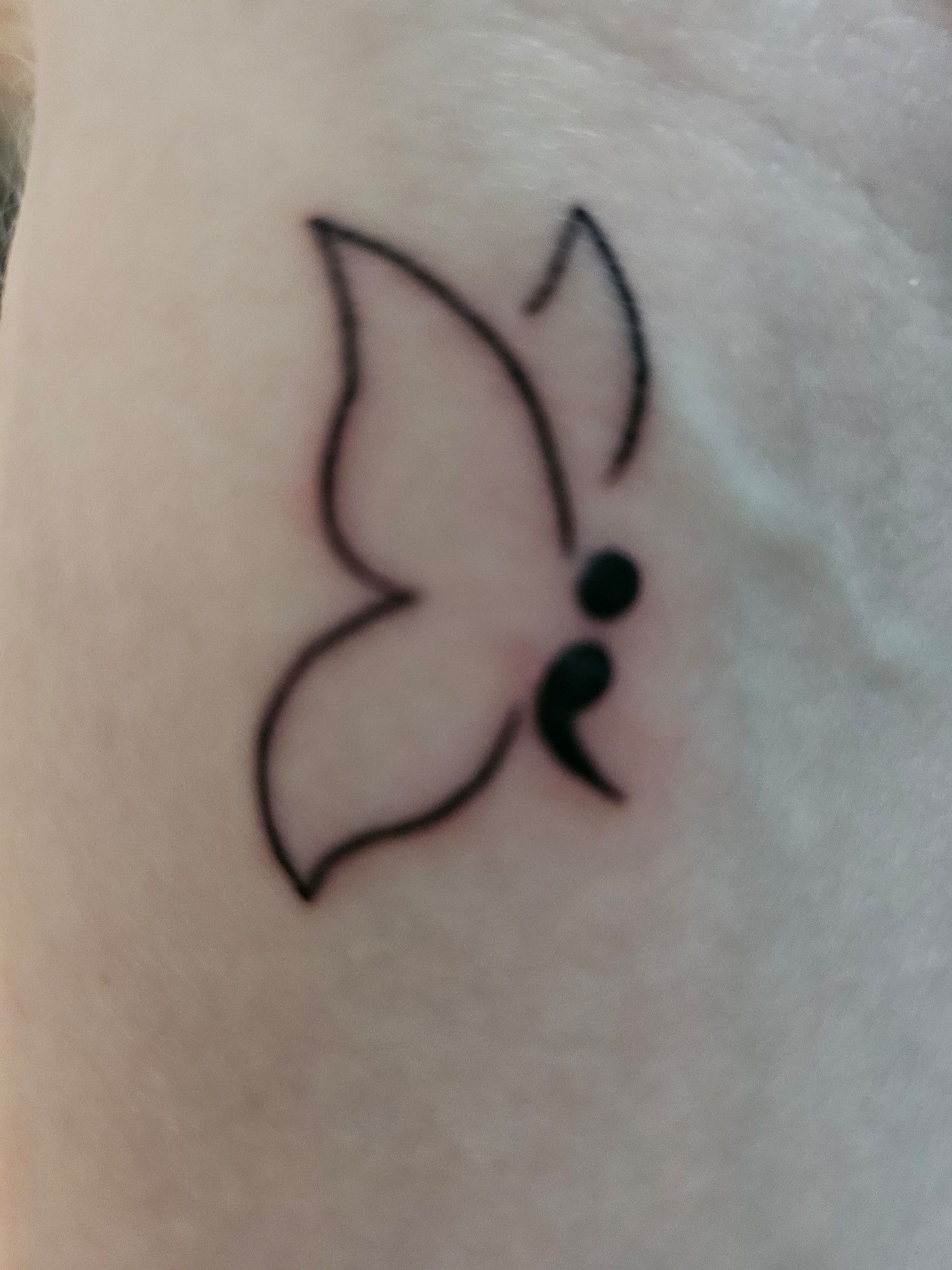 a semicolon butterfly tattoo below the left wrist