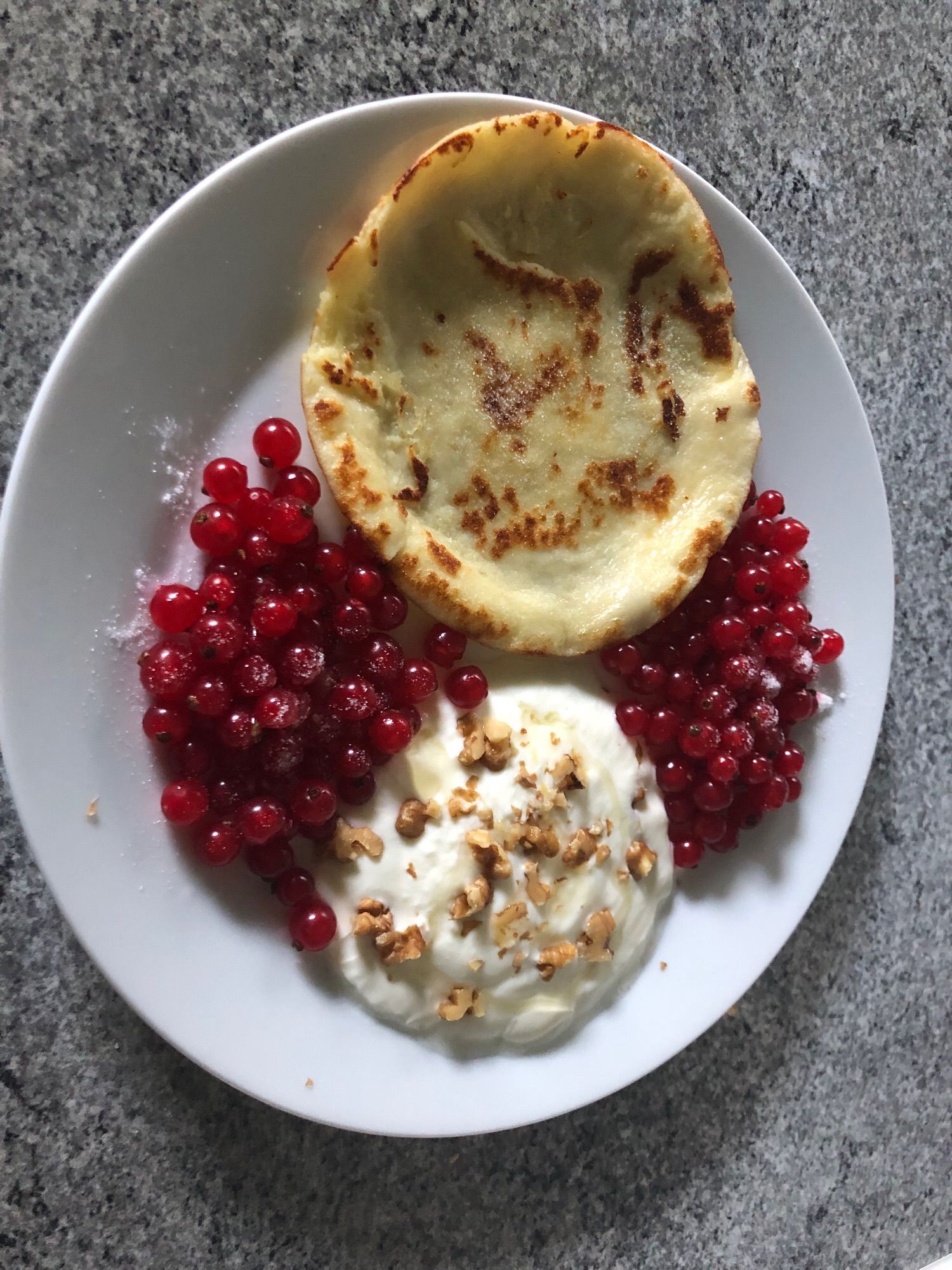 Ein kleiner Pfannkuchen mit Johannisbeeren & Yoghurt mit Walnuss-Honiggarnitur. Pfannkuchen und Beeren leicht gezuckert.