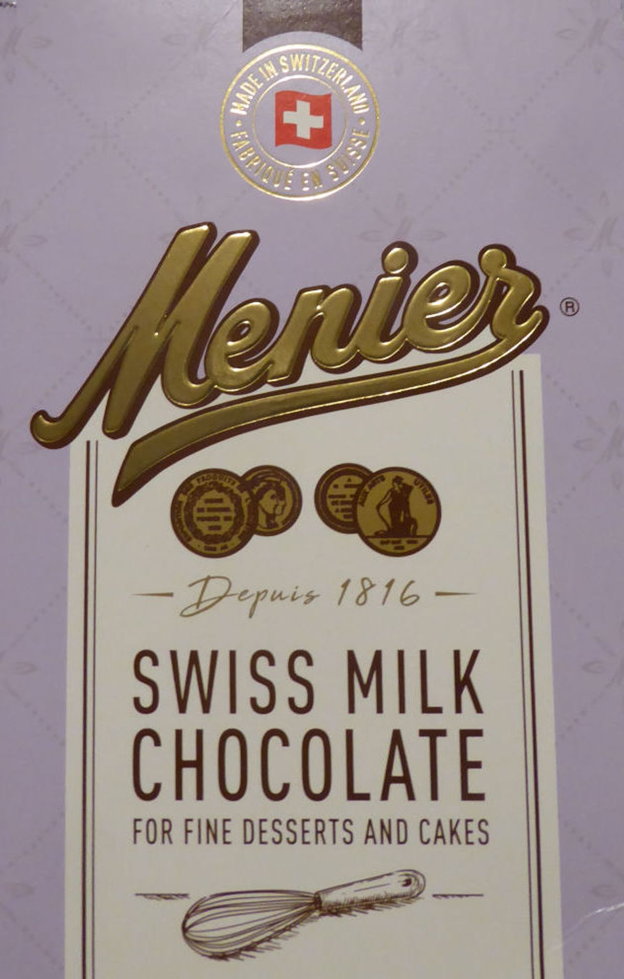 Packaging for Menier Swiss Milk Chocolate in golden, stylised letters, pale violet border with Swiss flag at top.