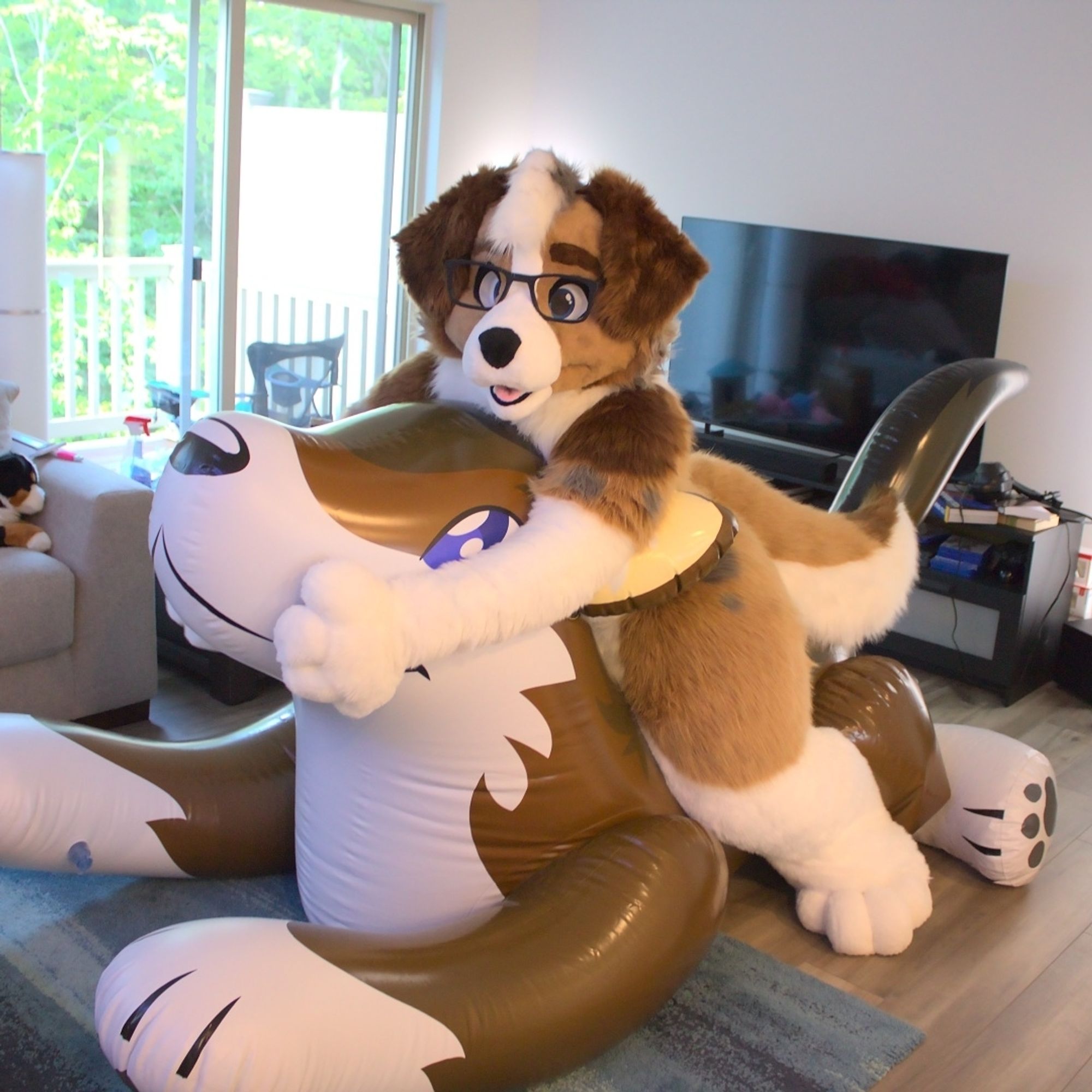 A floppy-eared dog fursuiter sitting on and hugging a brown wolf inflatable