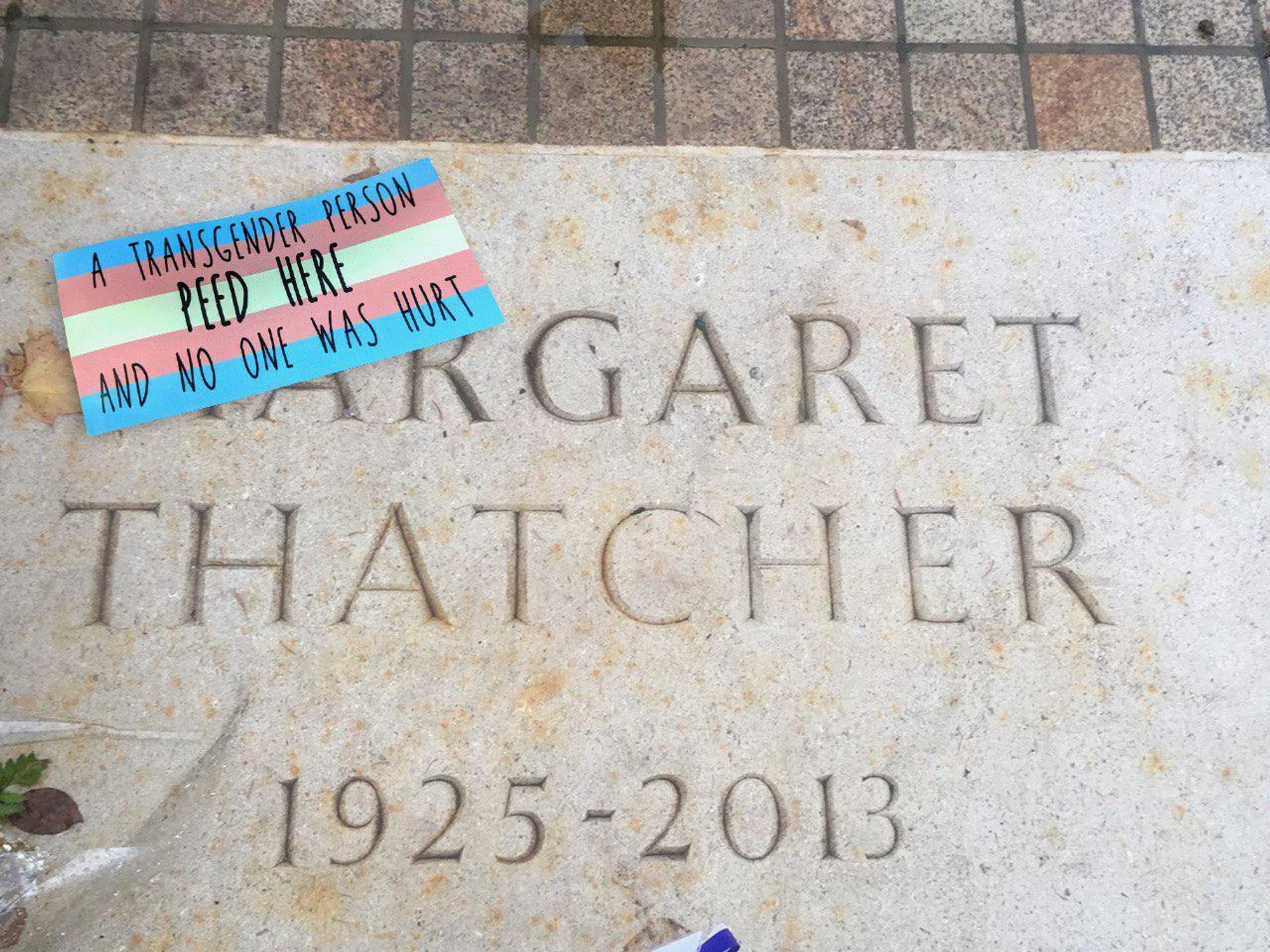 a sticker with a trans pride flag background, reading "a transgender person peed here and no one was hurt", attached to the grave of margaret thatcher