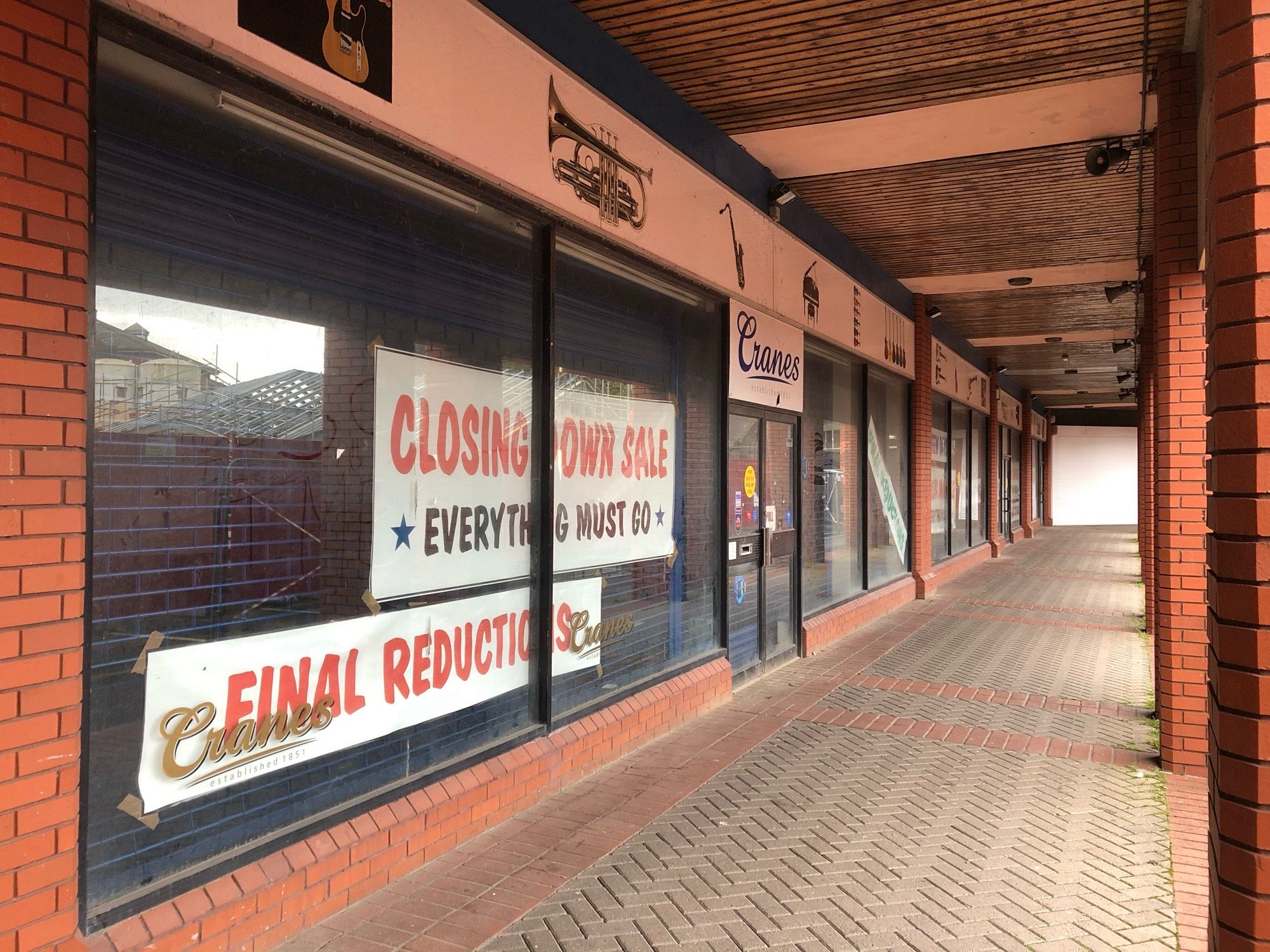 The closed-down Cranes music shop in the red-brick open-air St. David’s Shopping Centre in Swansea. Signs in the window say ‘Closing Down Sale, Everything Must Go’ and ‘Final Reductions’.