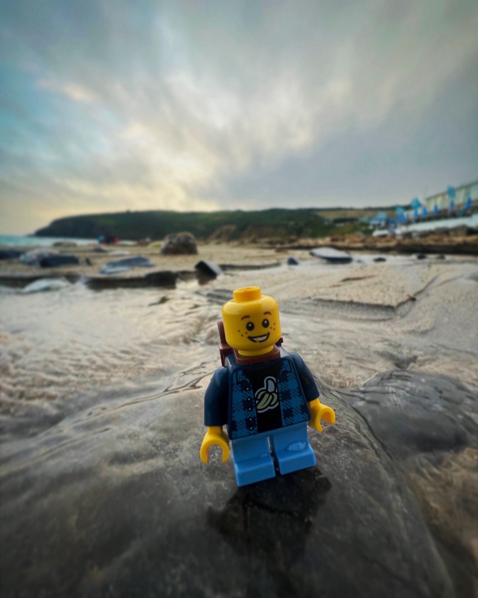 A image of a Lego mini figure on a beach, standing on a rock, water around him