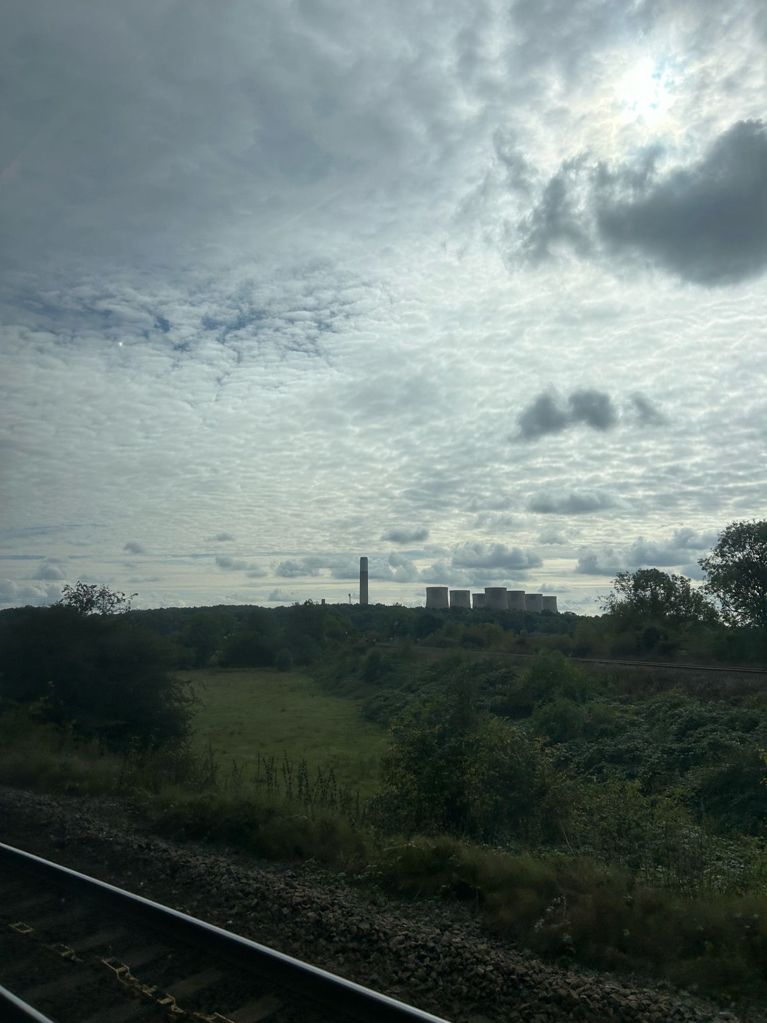 A chimney and cooling towers seen on the horizon against a cloudy sky. There is a railtrack in the foreground.