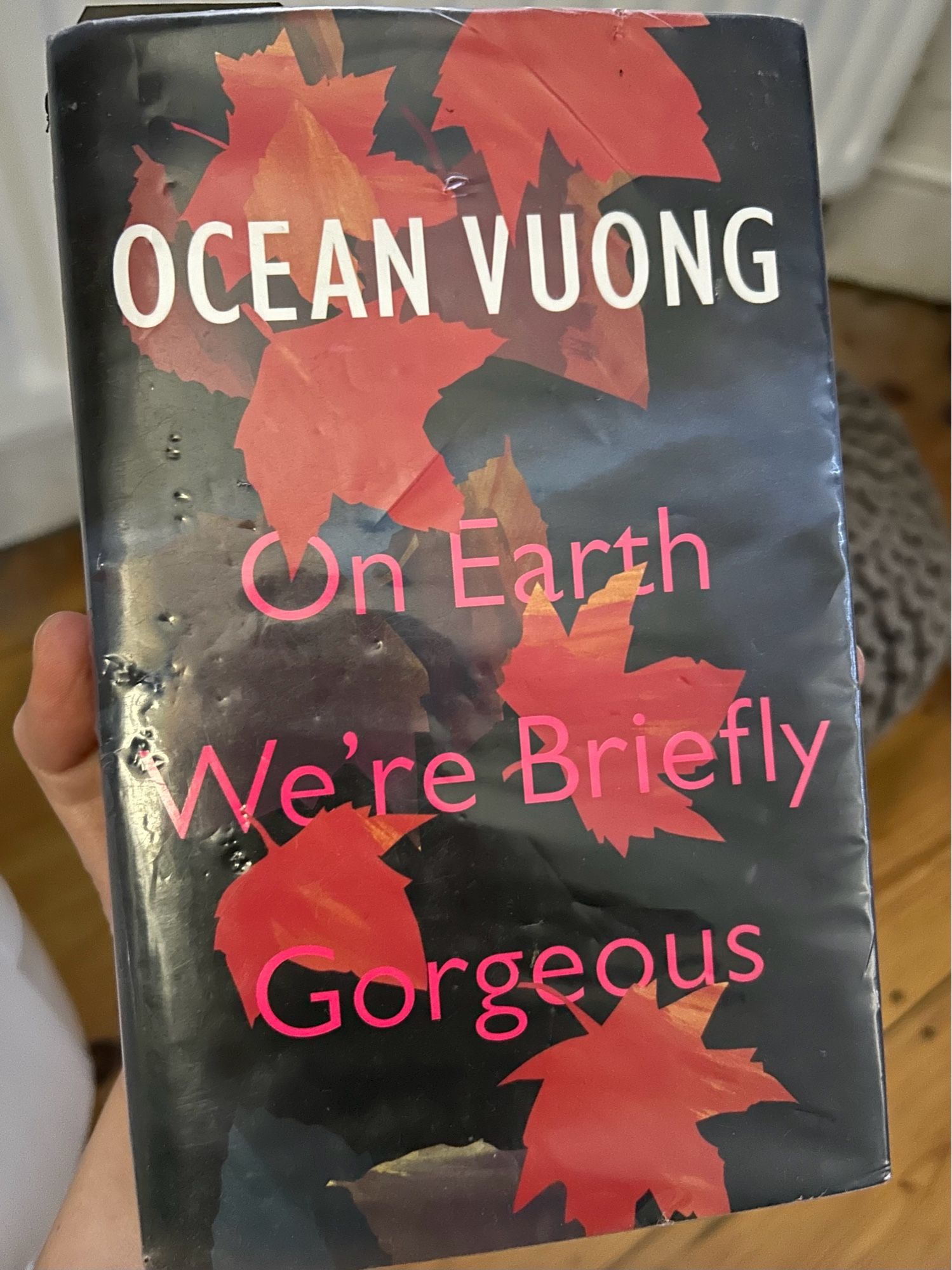 Library book with protective cover over a dark background and falling red leaves (Author: OCEAN VUONG; 
Title: On Earth We're Briefly Gorgeous)