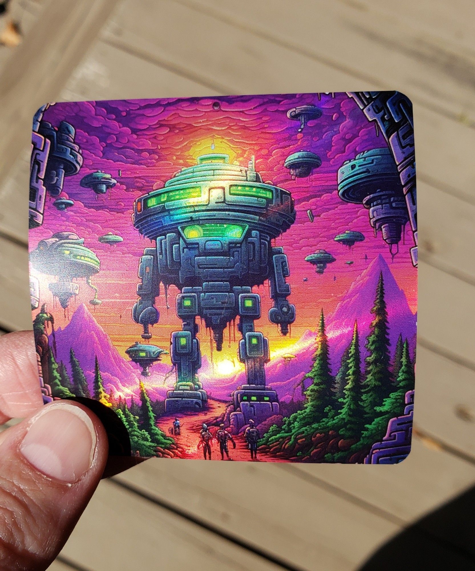 A shiny holographic sticker featuring a big robot and floating robots and purple mountains and a pink sky and green trees. It's exactly the kind of sticker you'd expect to get from a cannabis dispensary.