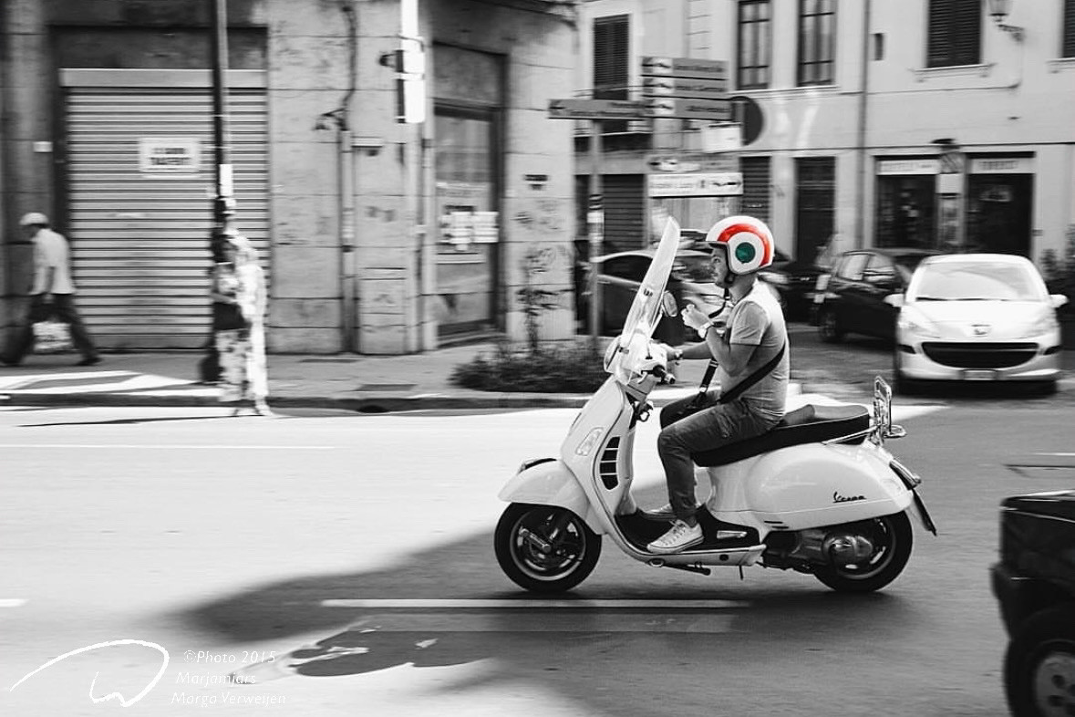 Quick snap in the streets of Palermo of a man on a Vespa scooter, wearing a helmet with circular design in colors of the Italian flag.