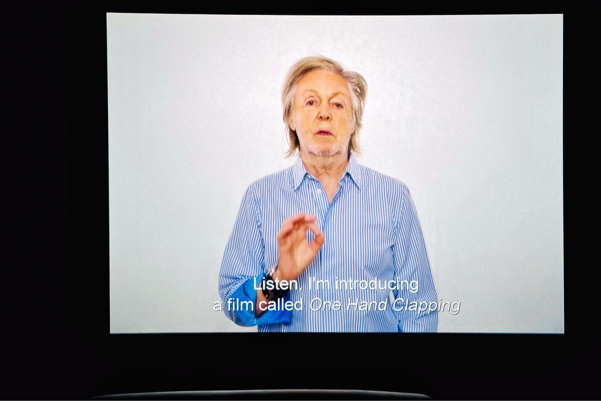 Cinema screenshot with Paul McCartney introducing the film ‘One hand clapping’. A small curved white line is an empty seat in front of me.