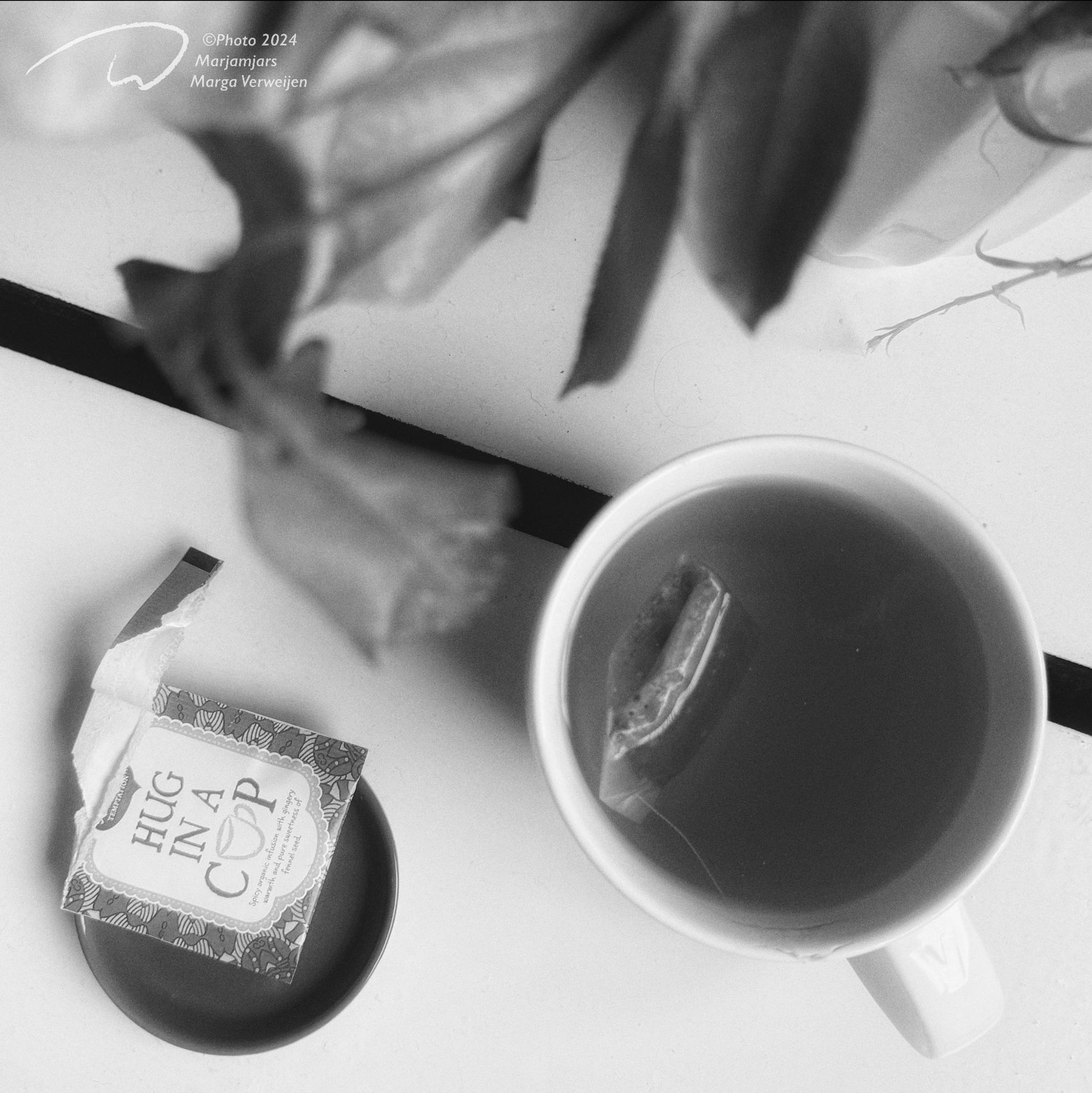 Table with a long dead and dried out flower bouquet a cup of tea and its original packaging with text that says ‘Hug in a Cup’. Exactly what I need. 😉