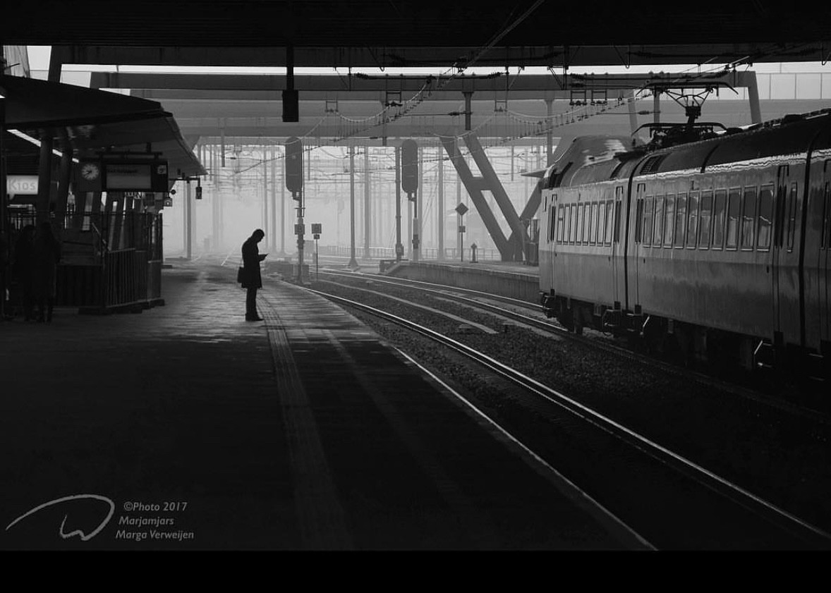 Empty train station with just one passenger waiting under the roof in the distance looking at phone. On right side a train is standing.