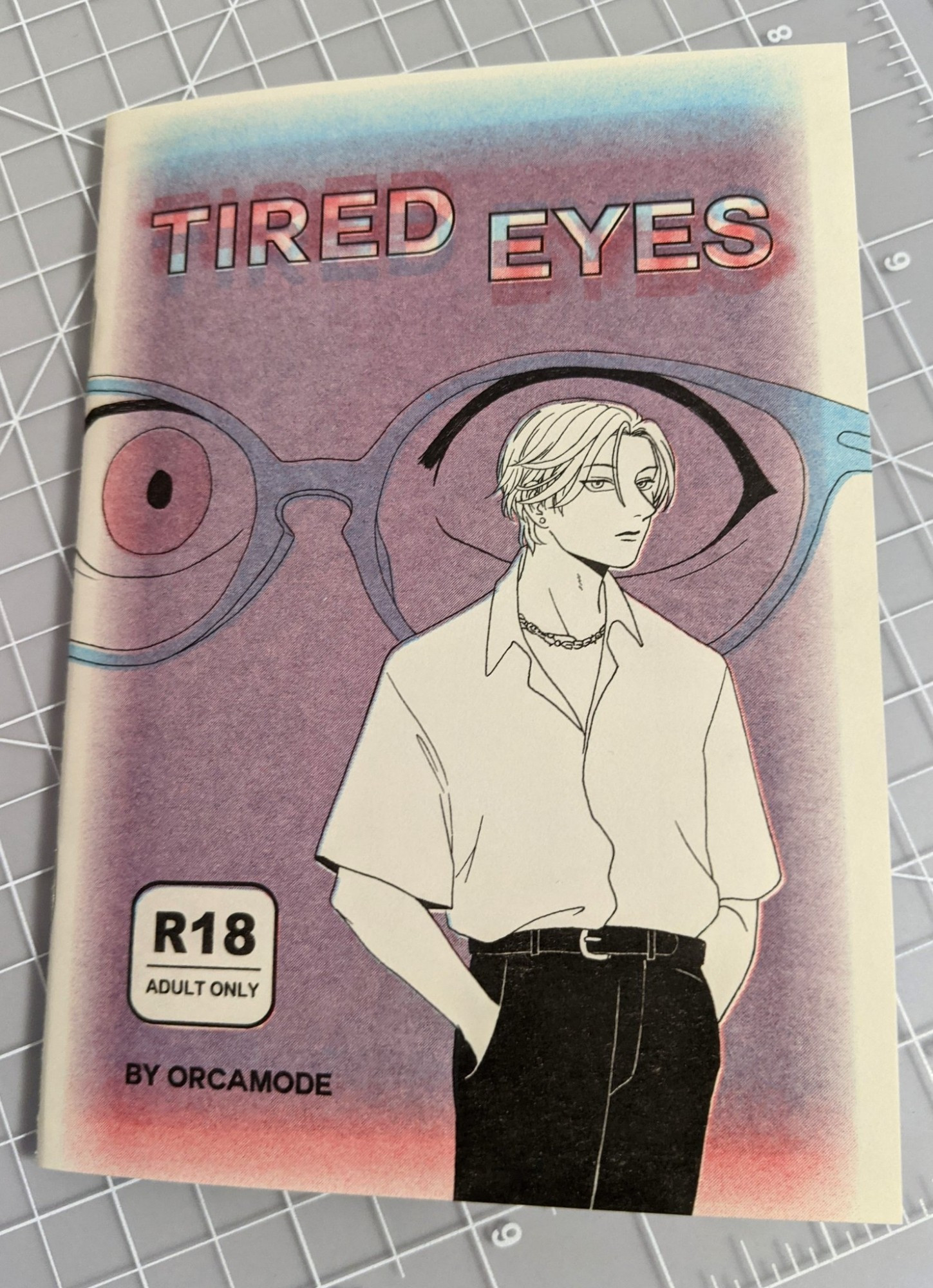 Cover of TIRED EYES by orcamode. A black-and-white drawing of a pretty man with a distant expression is imposed over a large pair of eyes watching him