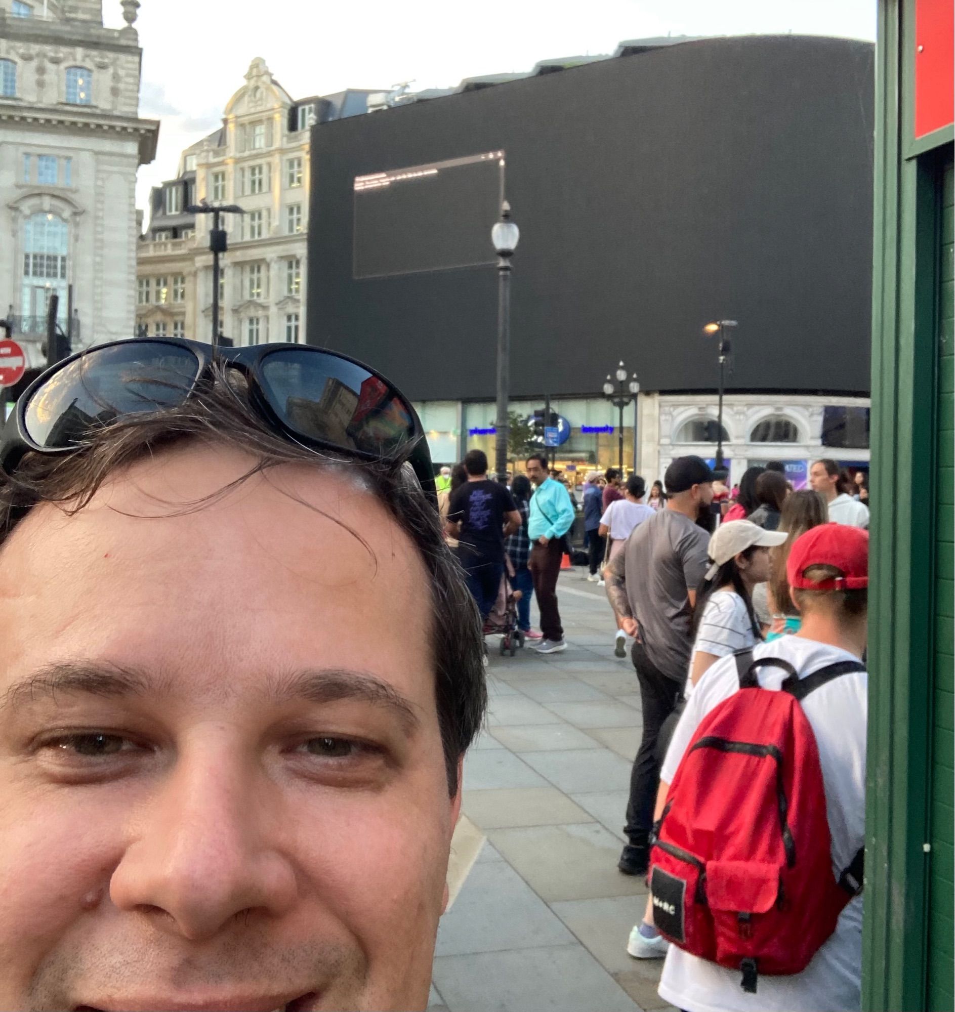 Selfie of Belouve with Piccadilly Circus sign in background, which is malfunctioning with a black screen and command line console.