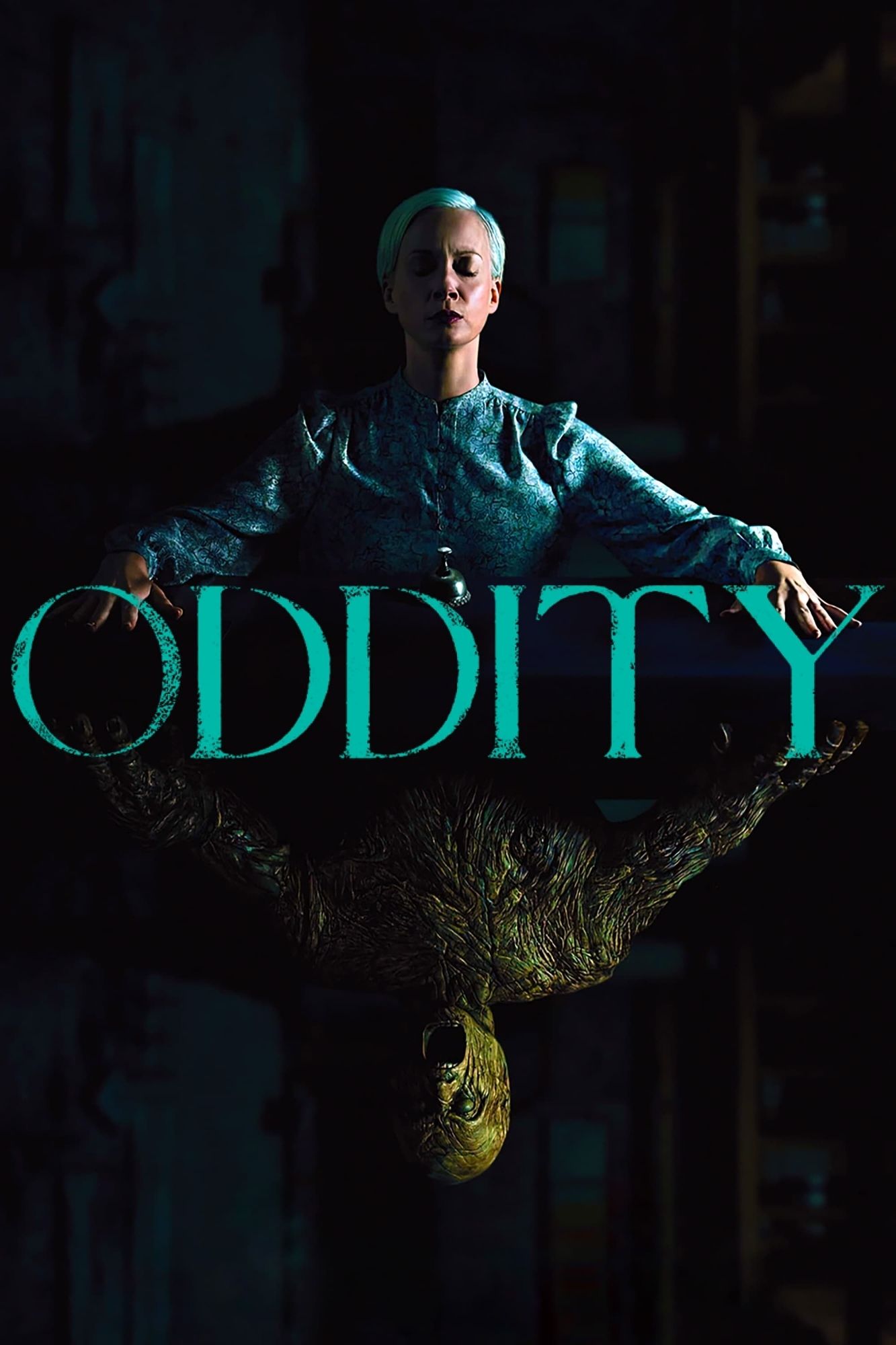 The poster for the horror movie Oddity. On top of a title a woman with short white hair wearing a blue dress sits with eyes closed and hands atop a table. Below the title, upside down but mirroring her pose, is an unsettling wooden sculpture of a person whose mouth gapes open in a snarl or scream