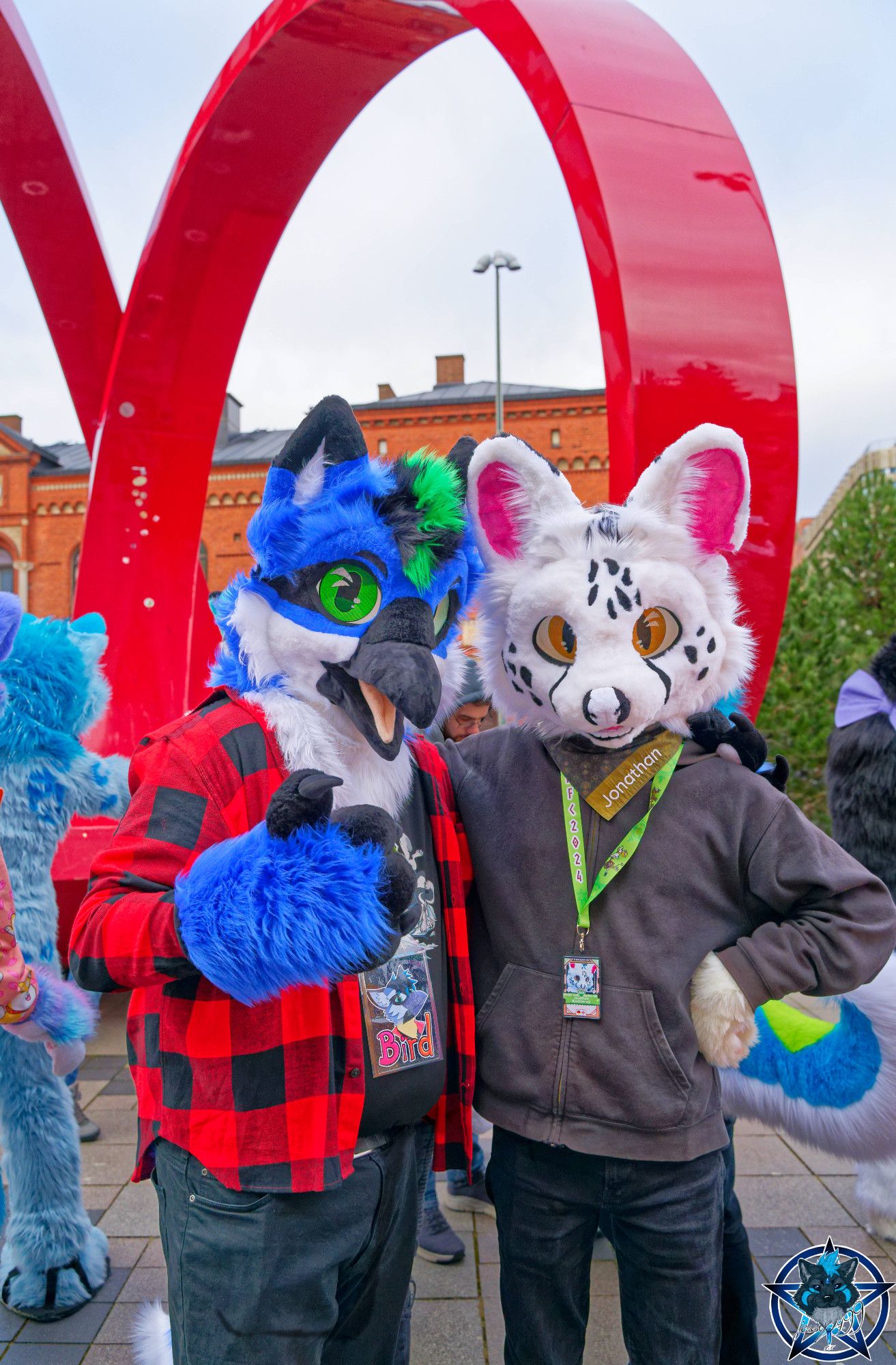 Photograph of a white serval fursuiter standing next to a blue bird fursuiter.