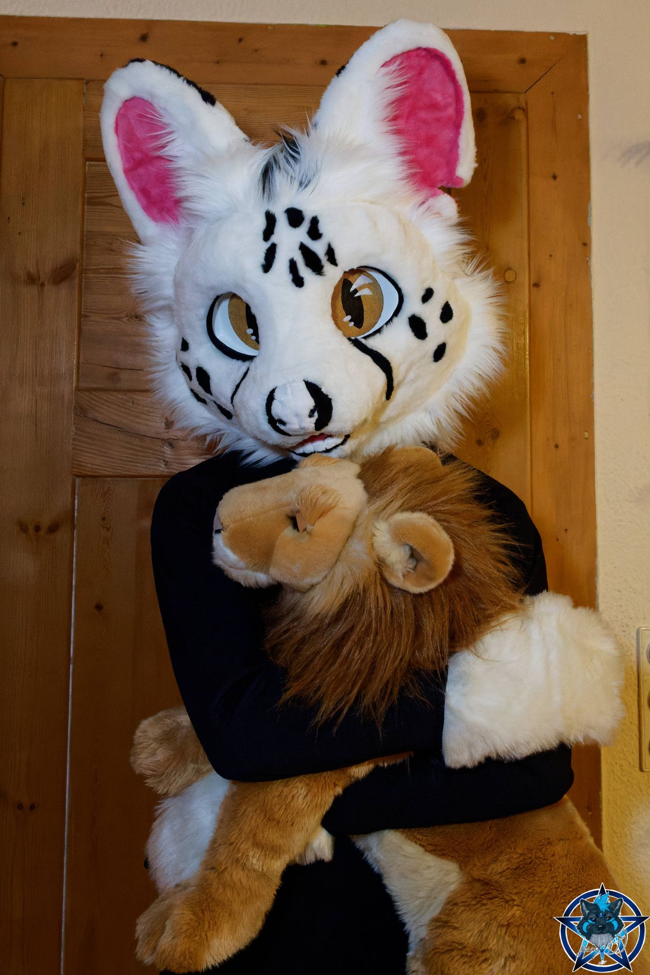 A serval fursuiter hugging a lion plush animal.