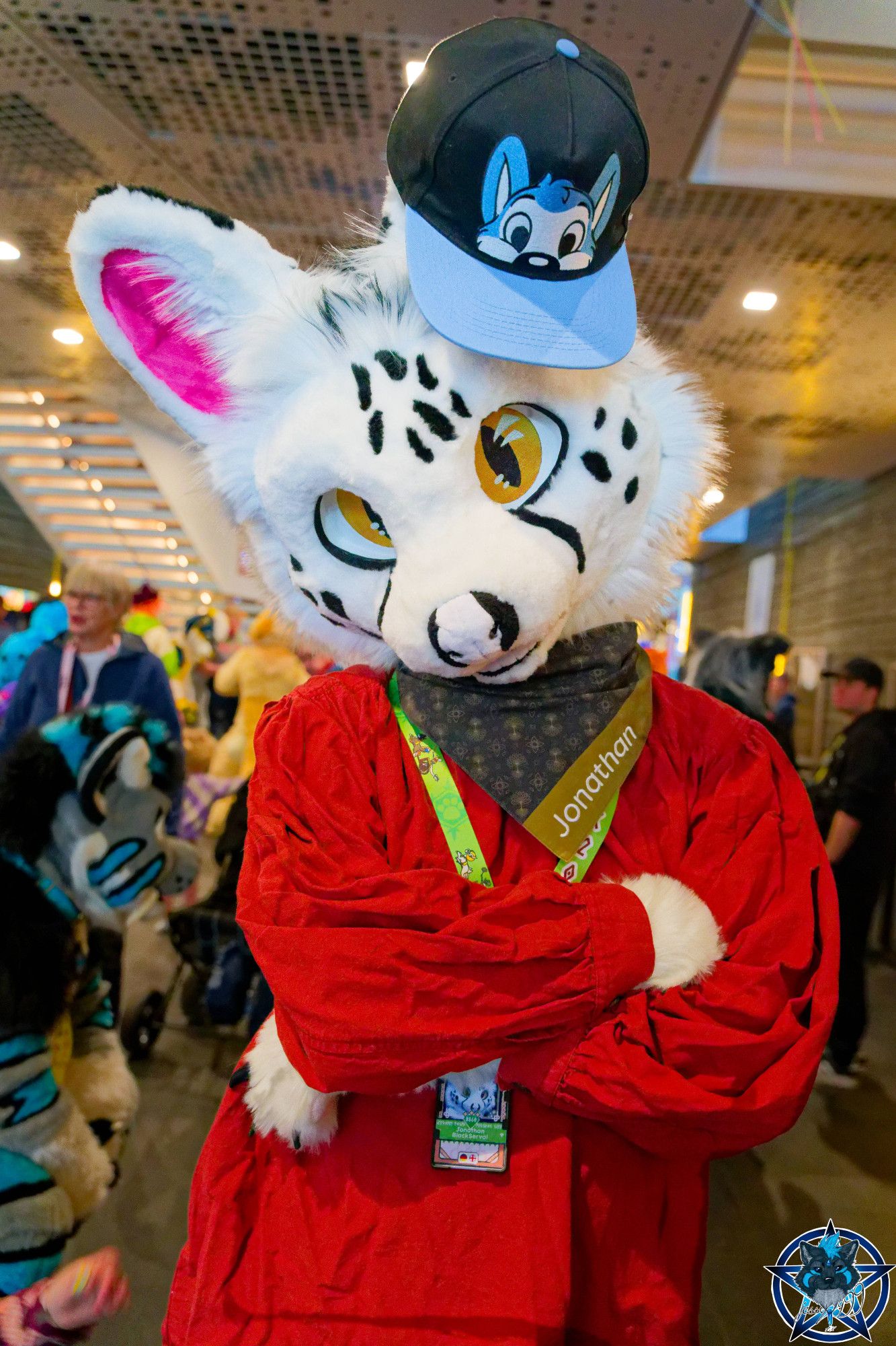 Photo of a white serval fursuiter wearing a peekabu cap.