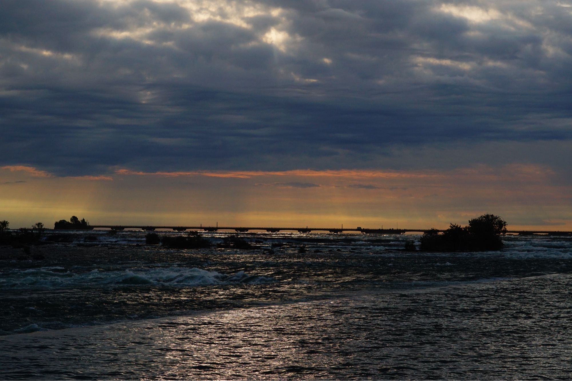 Sunrise over rapidly moving water with a bridge in background