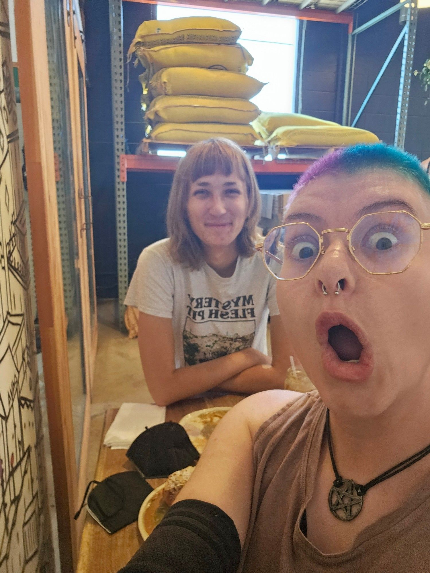 Adolin and Wednesday went on a cute coffee date! Adolin is a white nonbinary person with a nose ring, glasses, and a shaved head split dyed with pink and blue. Wednesday is a white nonbinary trans fem with a blonde bob. She smiling the the photo.