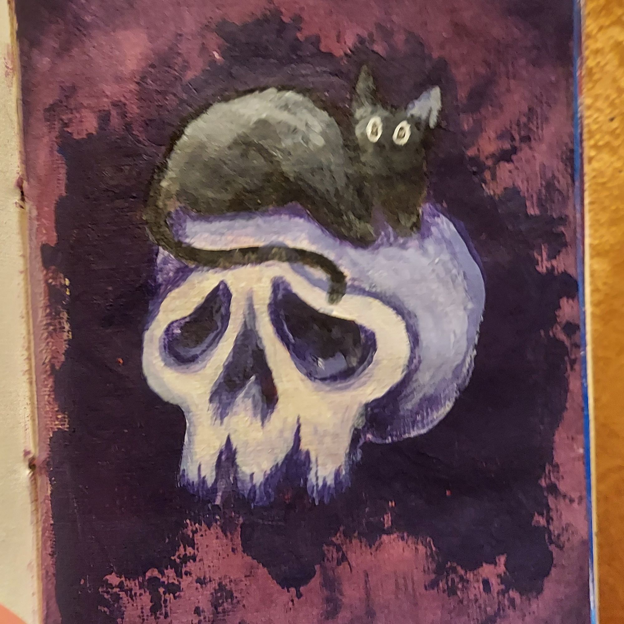 A painting of a skull with a black cat laying on the top.