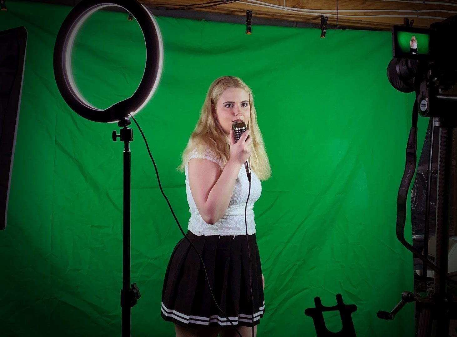 Tara St. Michel shooting a video with a ring light and green screen singing into a vintage microphone