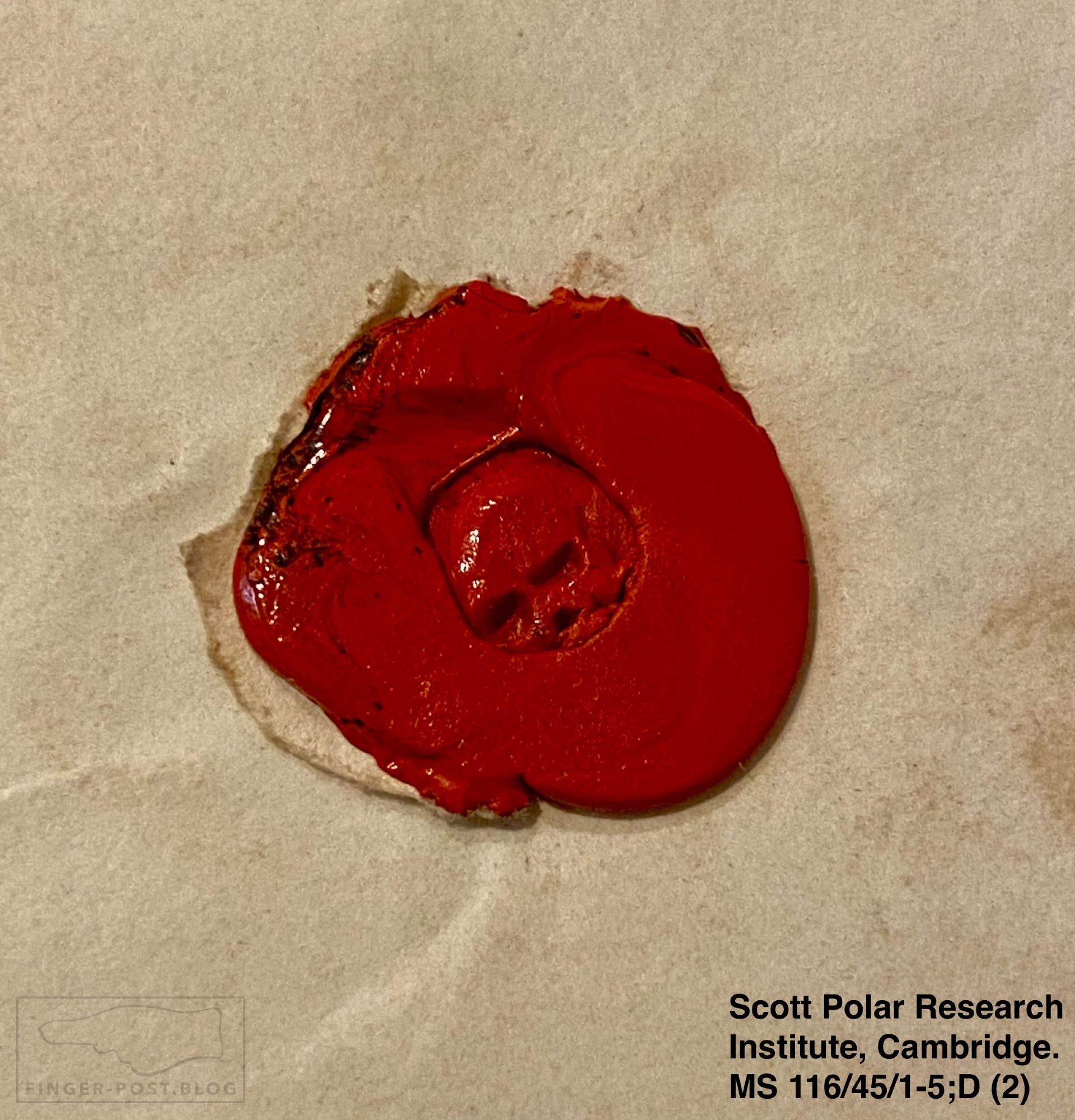 Image shows a roughly circular blob of bright red sealing wax. In the centre of the wax is the impression of a human skull.