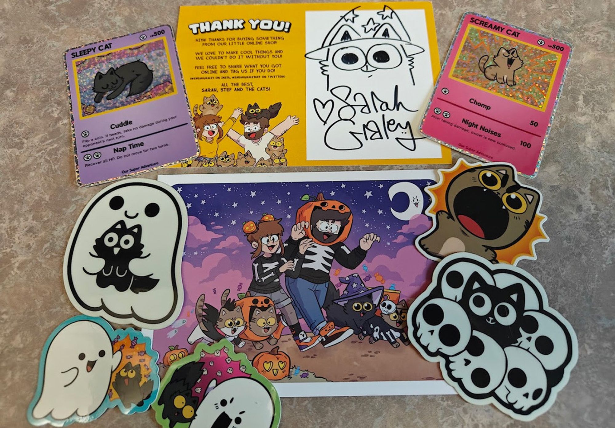 Sticker haul from Our Super Adventure webcomic from Tumblr featuring two pokemon themed stickers, a ghost hugging a black cat, a screaming cat, a cat with skulls, two colorful ghost stickers, a bonus sketch thank you card, and a bonus art postcard.