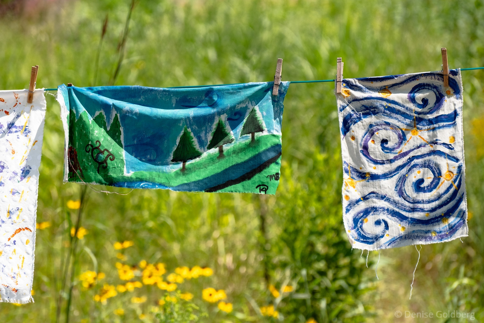 a mural painted on cloth showing trees on a hill of grass with a background of blue / cyan as the sky