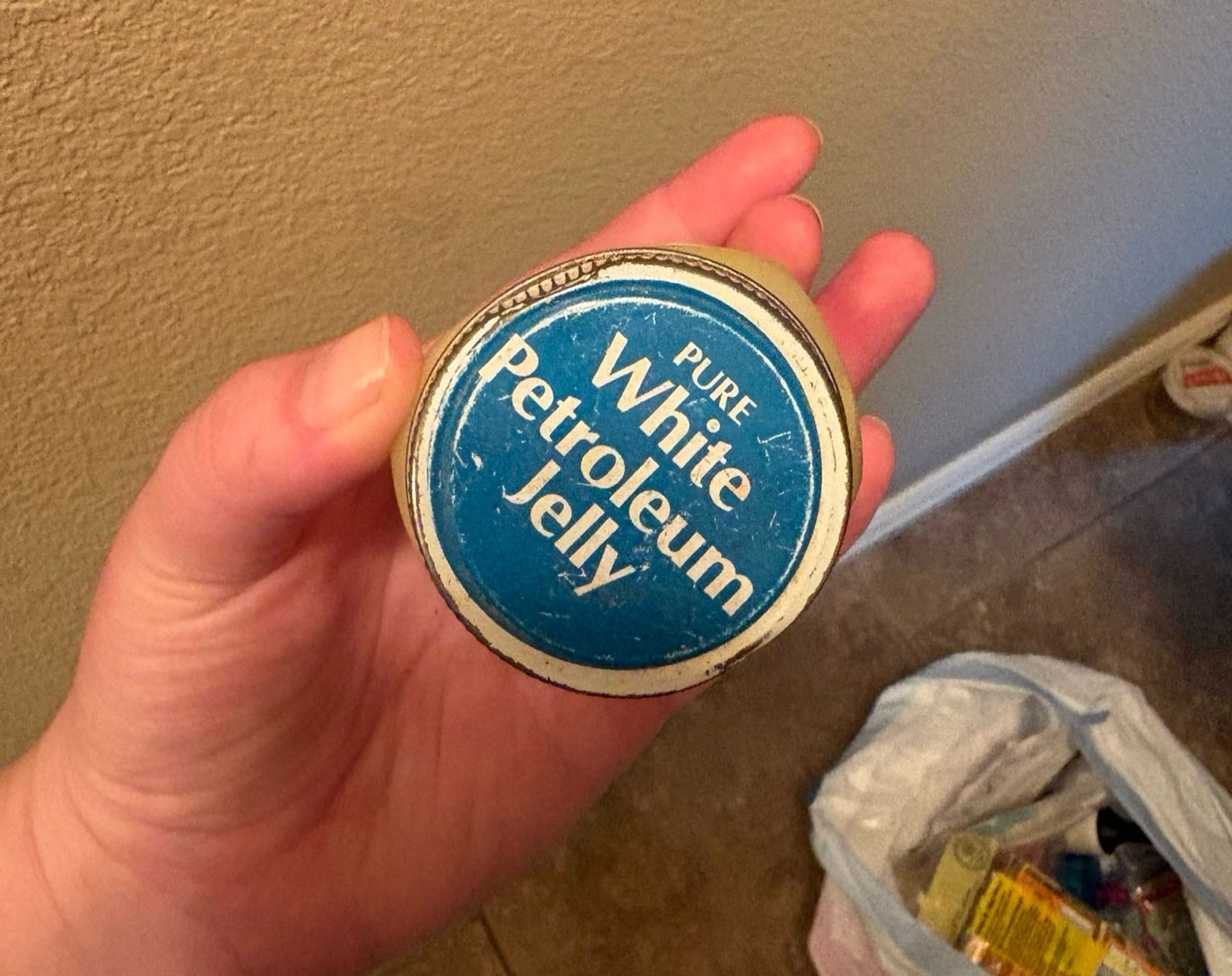 The lid of a very old jar of pure white petroleum jelly blue background with white lettering in a left hand in a house