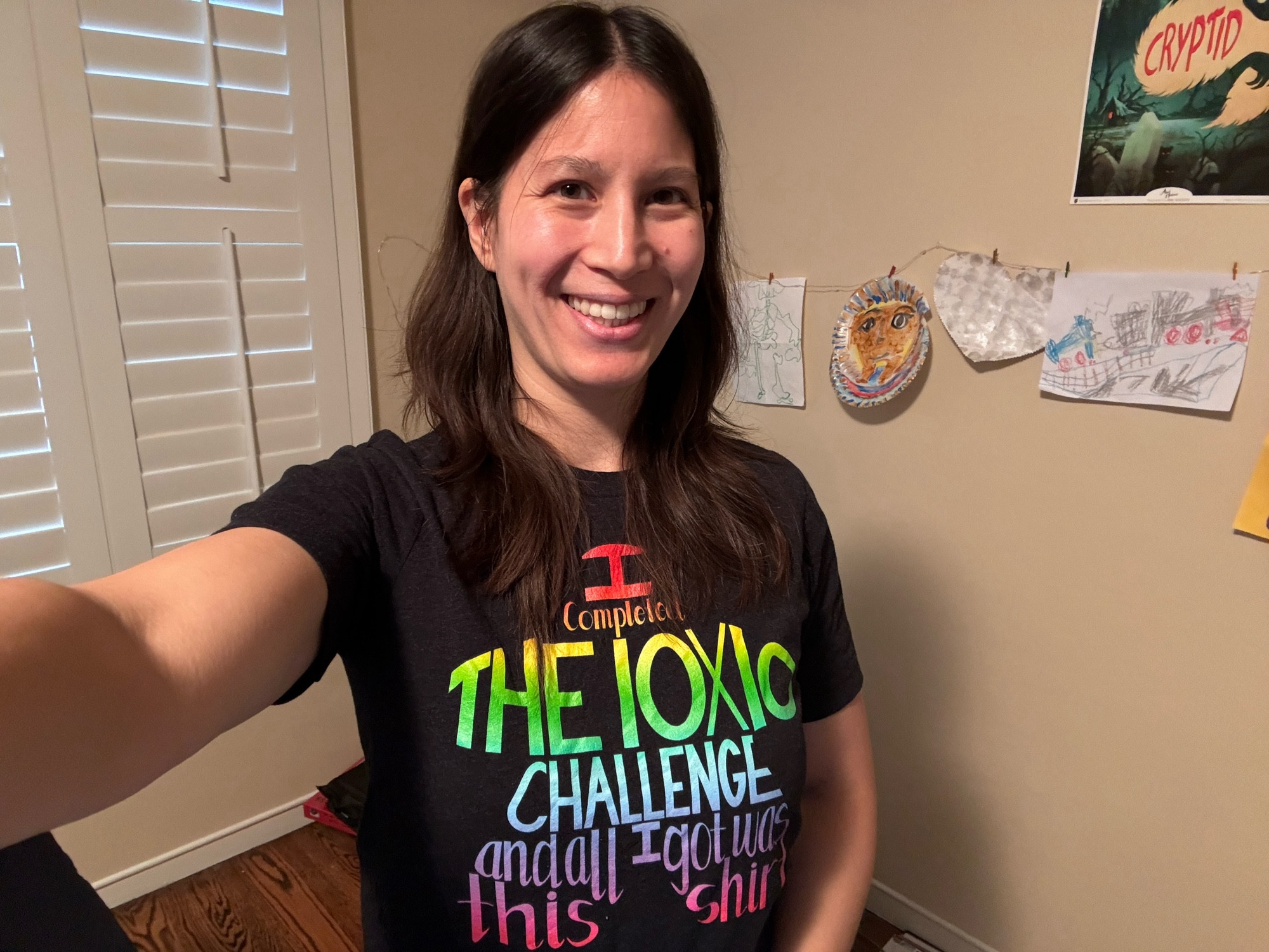 Me wearing a tshirts with rainbow text in the shape of a meeple: “I completed the 10x10 challenge and all I got was this shirt”