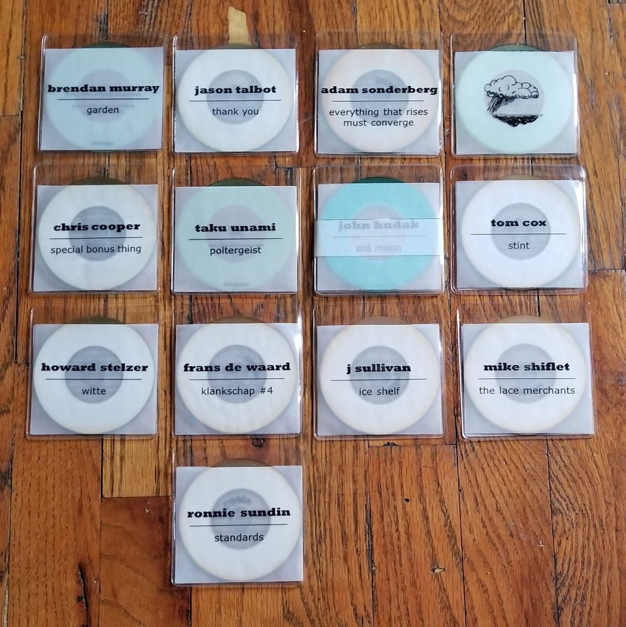 a group of 3" CD-rs laid out in a grid on a wood floor. each is in a clear vinyl sleeve with similar simple covers: a square of vellum with centered text - the artist's name in bold, a centered line divider, and the album title below. with the exception of Mike Bullock's disc which is a b&w drawing of rain pouring from a cloud over a flat landscape

l to r, top to bottom:

Brendan Murray - garden
Jason Talbot - thank you
Adam Sonderberg - everything that rises must converge
Mike Bullock - 'this will cheer you up'

Chris Cooper - special bonus thing
Taku Unami - poltergeist
John Hudak - old moon
Tom Cox - stint

Howard Stelzer - witte
Franz de Waard - klankschap #4
J Sullivan - ice shelf
Mike Shiflet - the lace merchants

Ronnie Sundin - standards