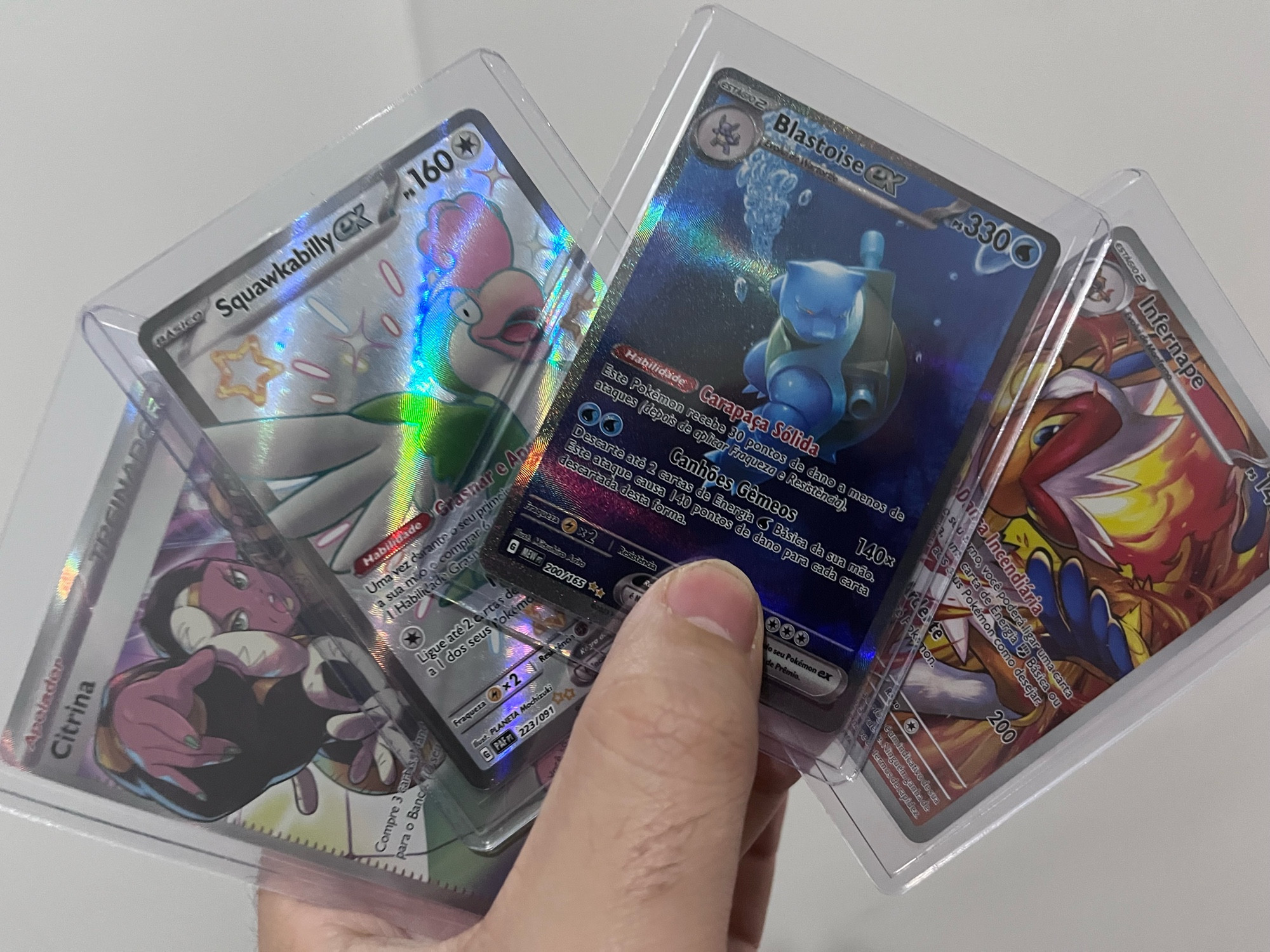 Quatro cartas de Pokémon TCG em cases de proteção. As cartas são A Treinadora Citrina, Infernape, Squawkabilly EX e Blastoise EX com arte alternativa 