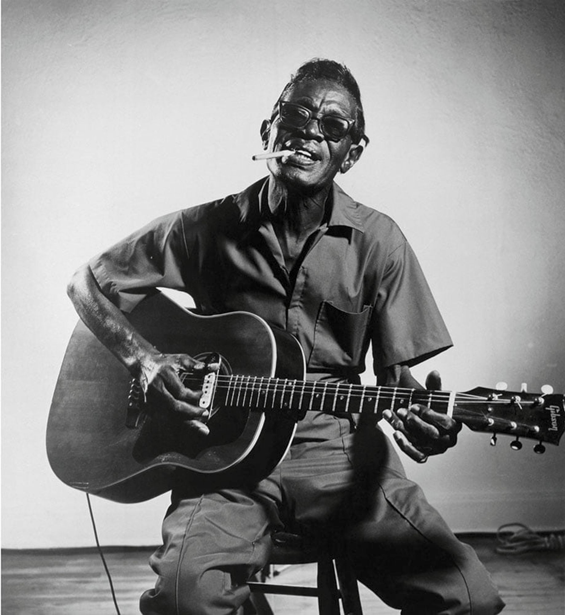 Photo de Lightnin Hopkins  (March 15, 1912 – January 30, 1982) avecsa guitare, lunettes noires et clopes au bec