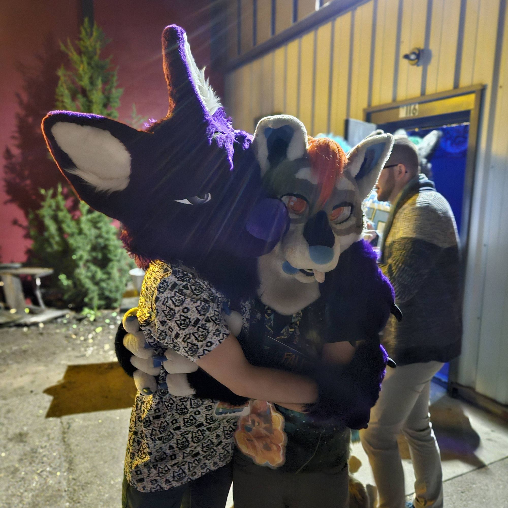 2 fursuiters hug each other outside a bar