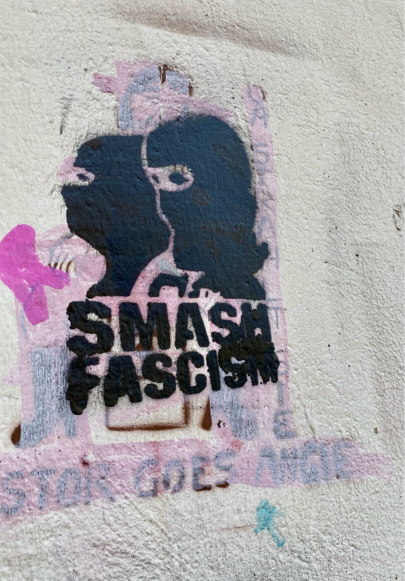 Ein Graffito auf dem in schwarzer Farbe stilisiert zwei maskierte Menschen zu sehen sind. Darunter steht in Großbuchstaben: „SMASH FASCISM“