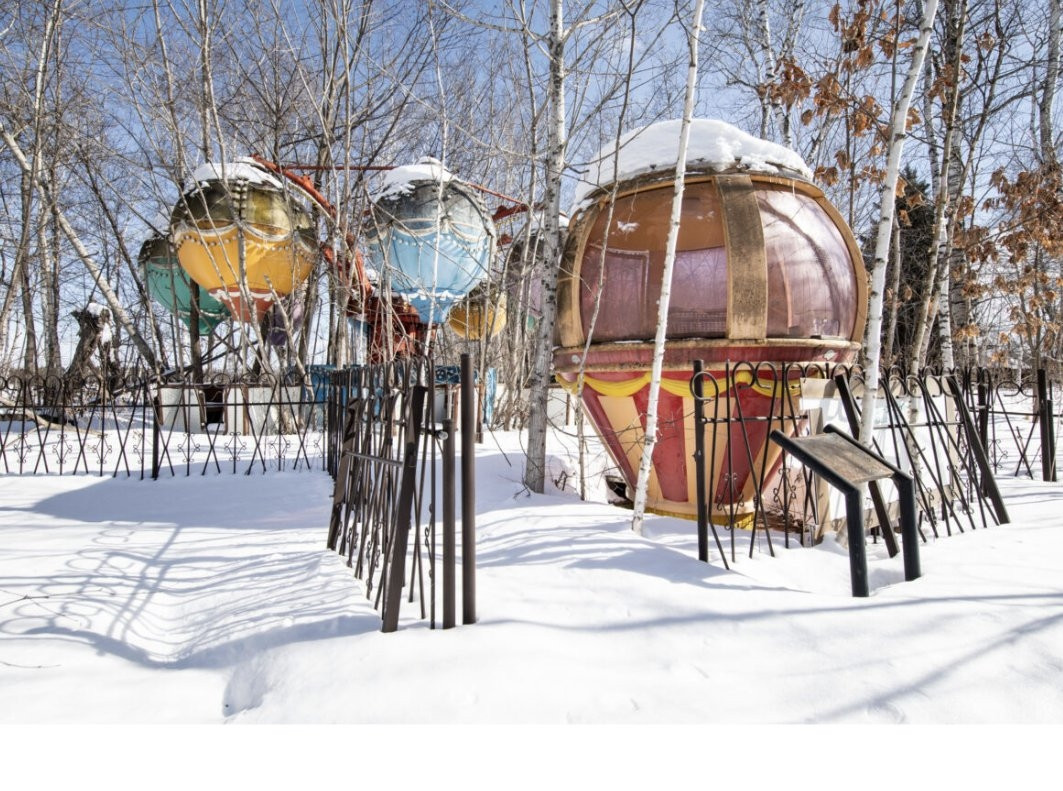 Photograph of an abandoned fairground ride in the snow.