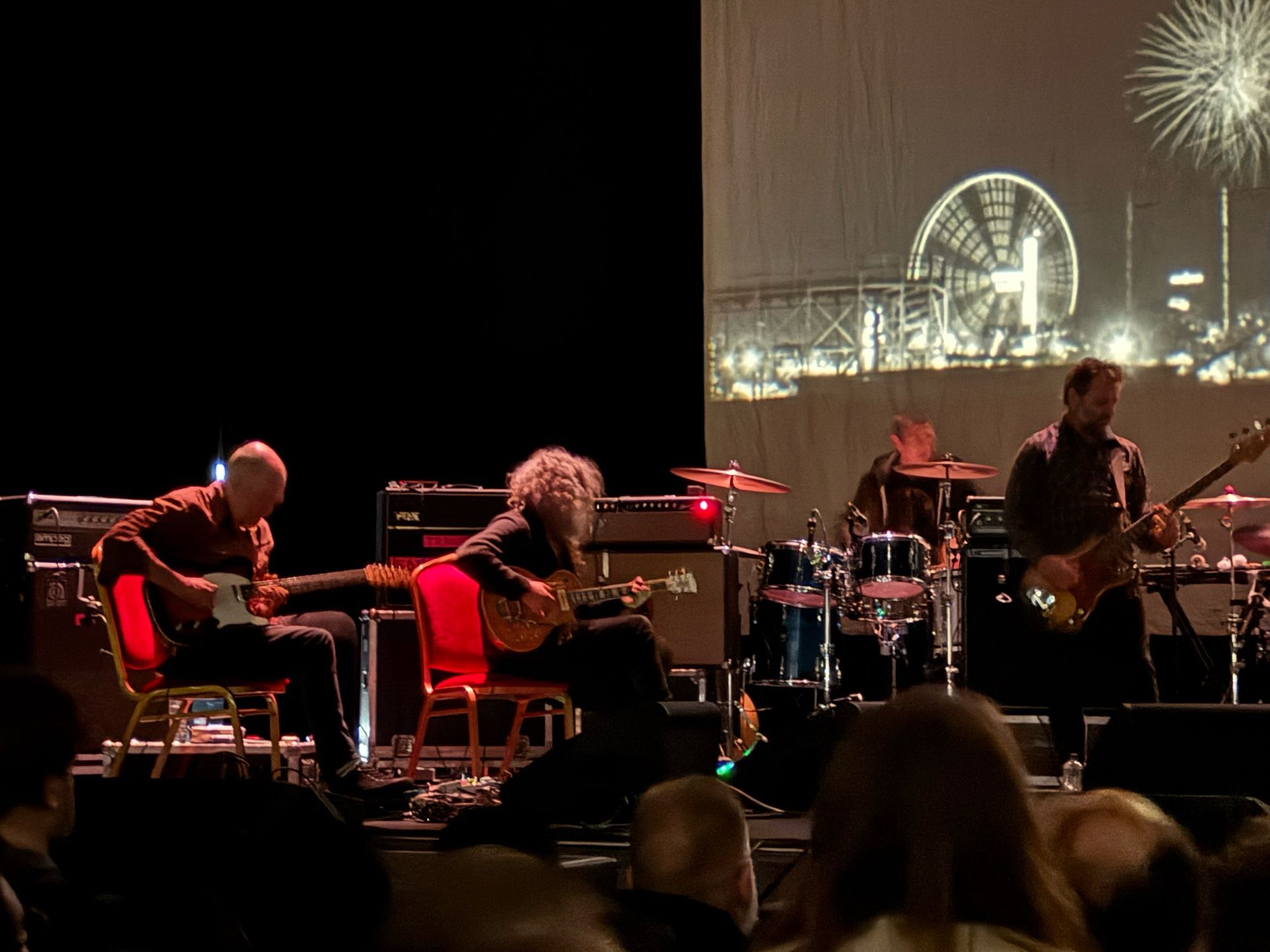 Godspeed, zoomed in on Mike Moya, Efrim & Mauro with a fairground image in black & white behind them, oh & Tim on drums.