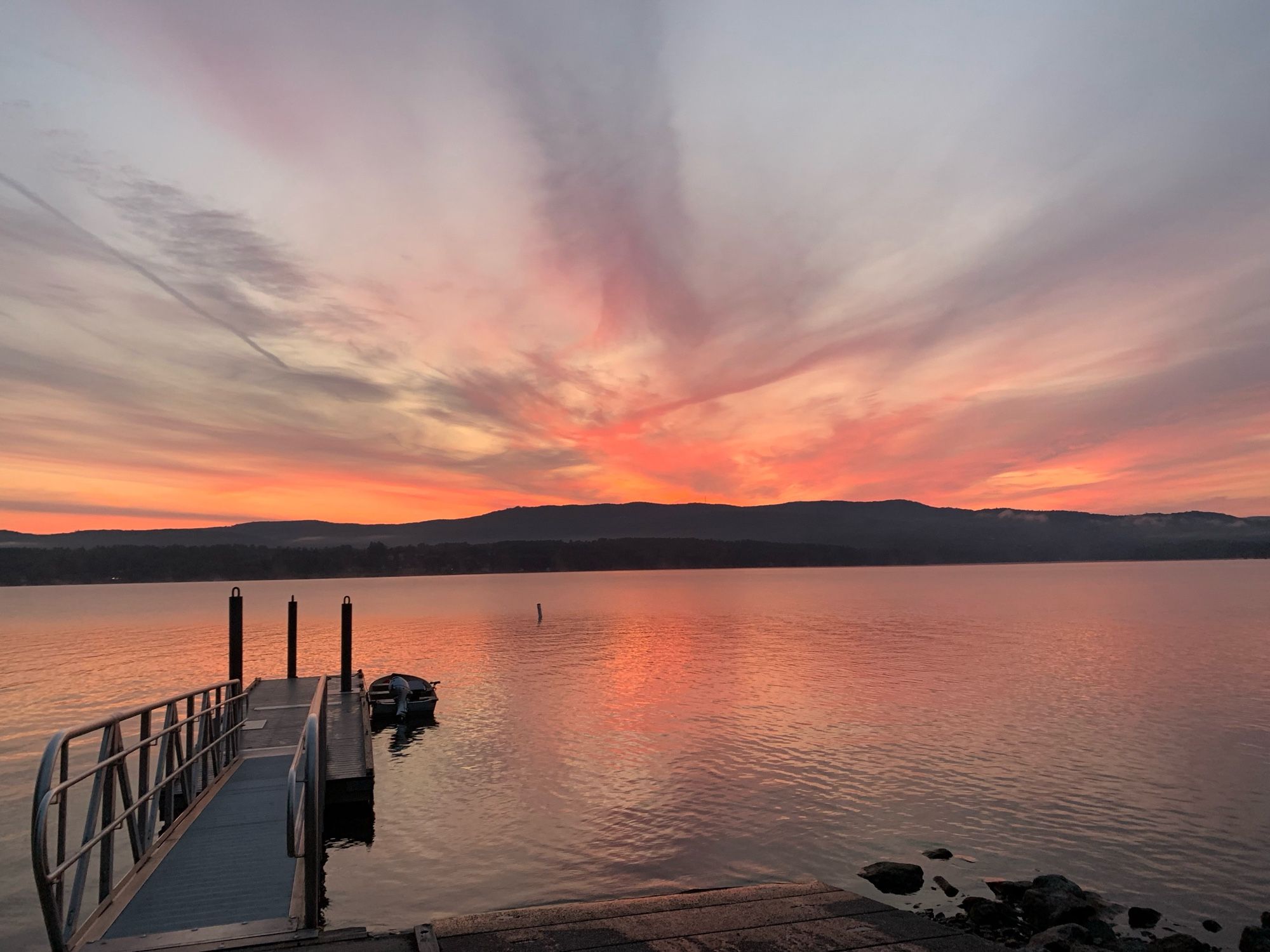 Sunrise through wispy clouds. Small boat tied to  the dock ready for fishing