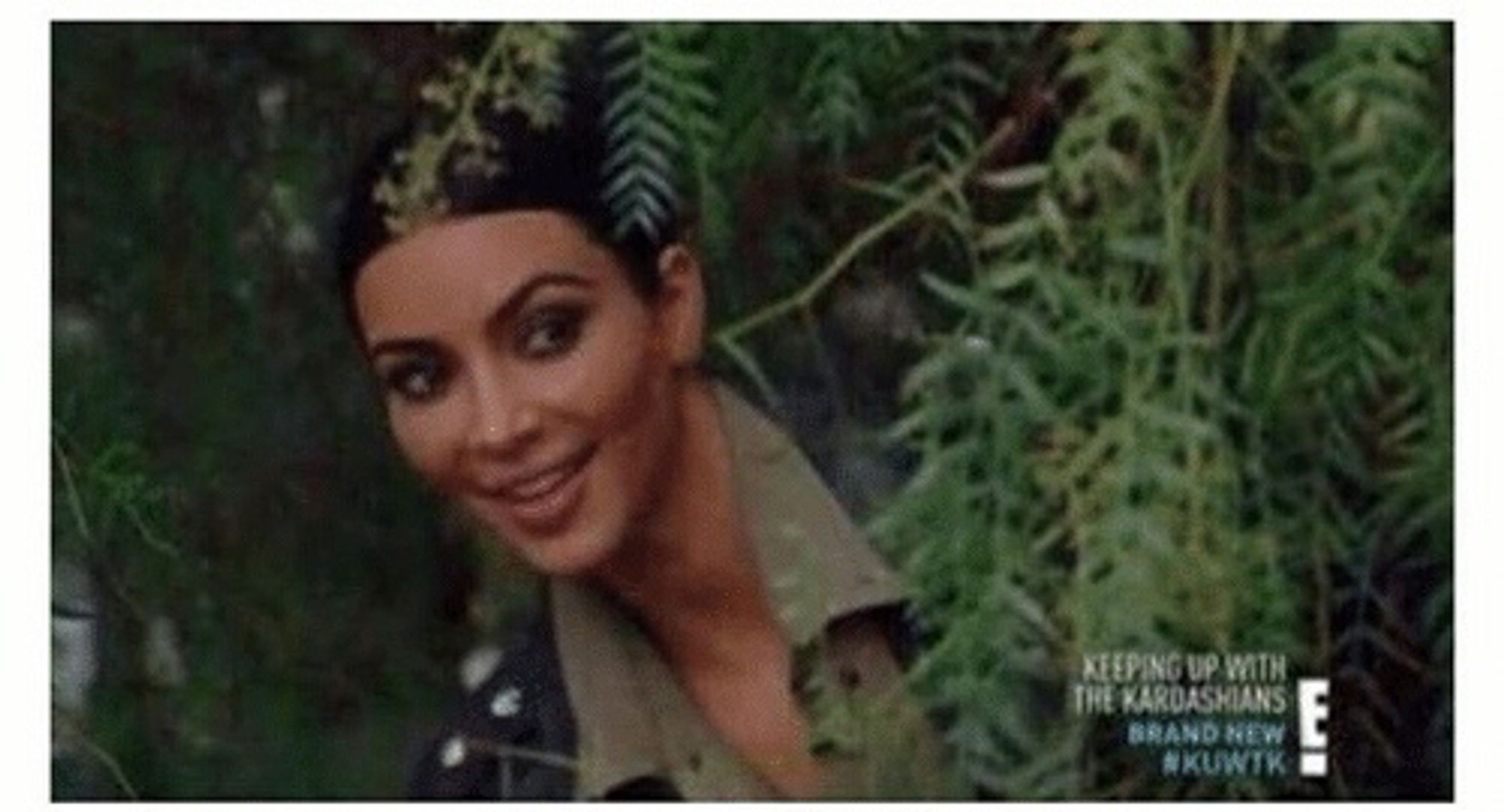 Kim Kardashian peeking at something from behind a bush.