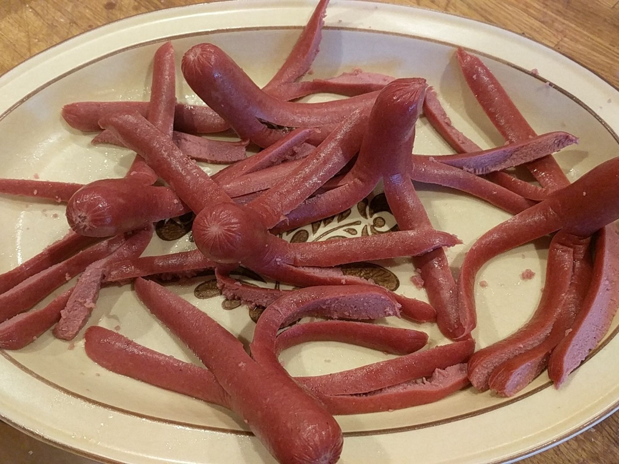 Six hot dogs on a plate, each with one end bisected into 8 long strips to look like the tentacles of an octopus: a hotdogtopi.