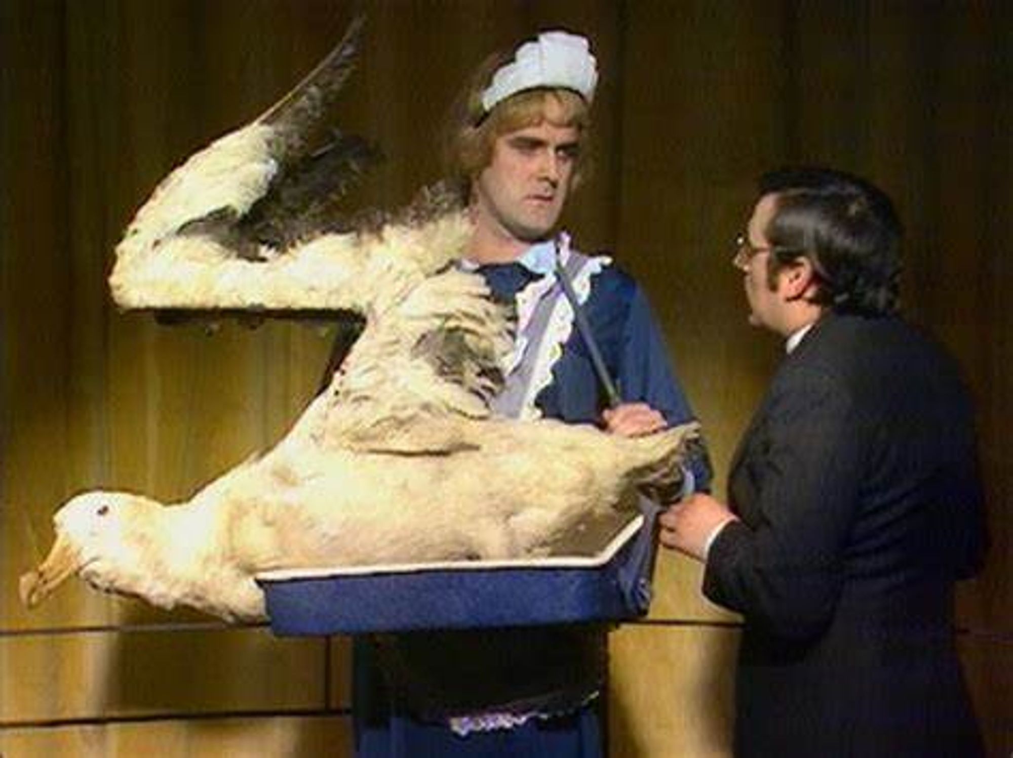 John Cleese dressed as a cinema usherette and carrying an albatross