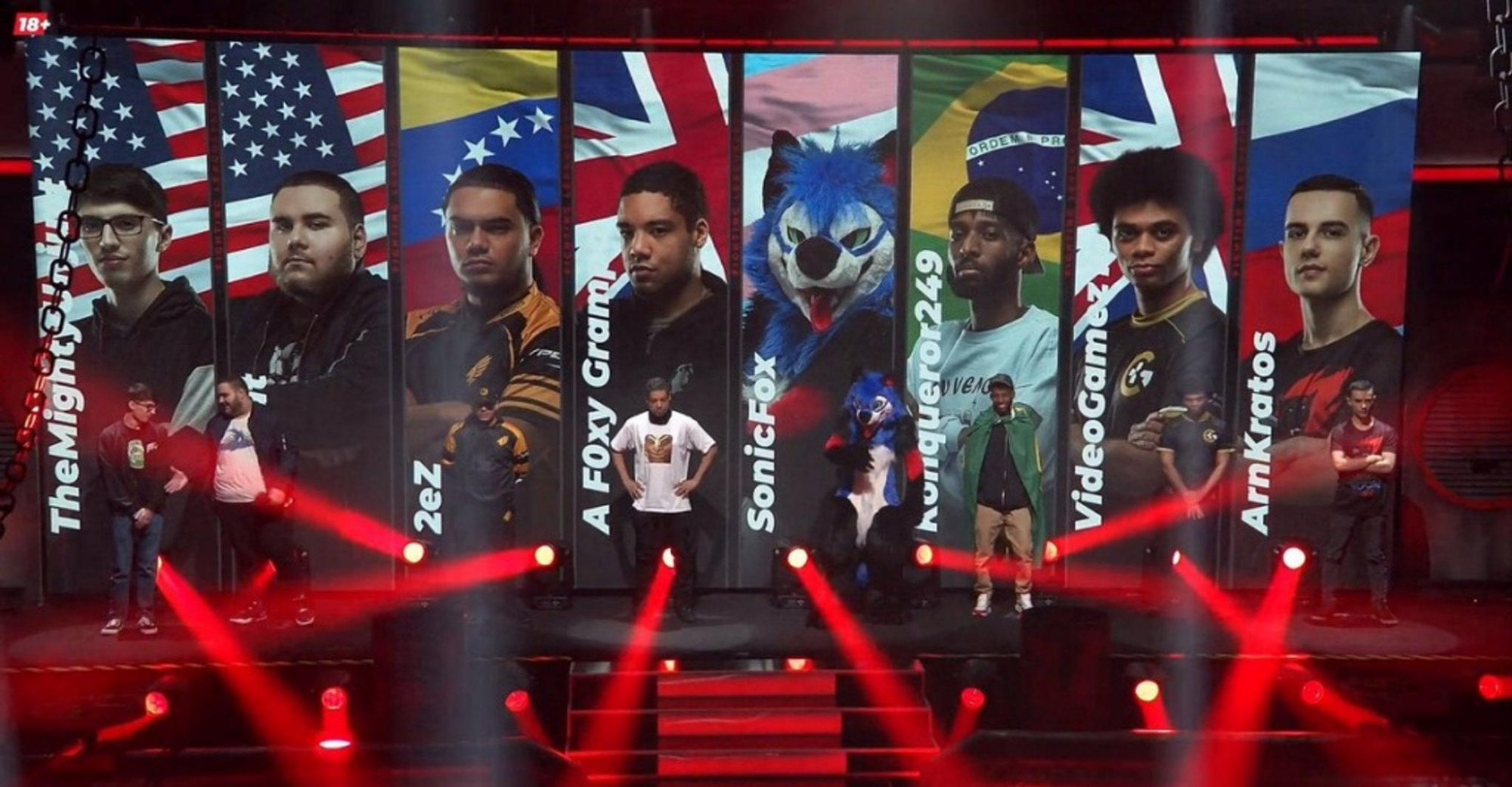 Line up of a pro gaming team with their flags in the background. One is a guy name SonicFox wearing a fur suit standing in front of the trans flag
